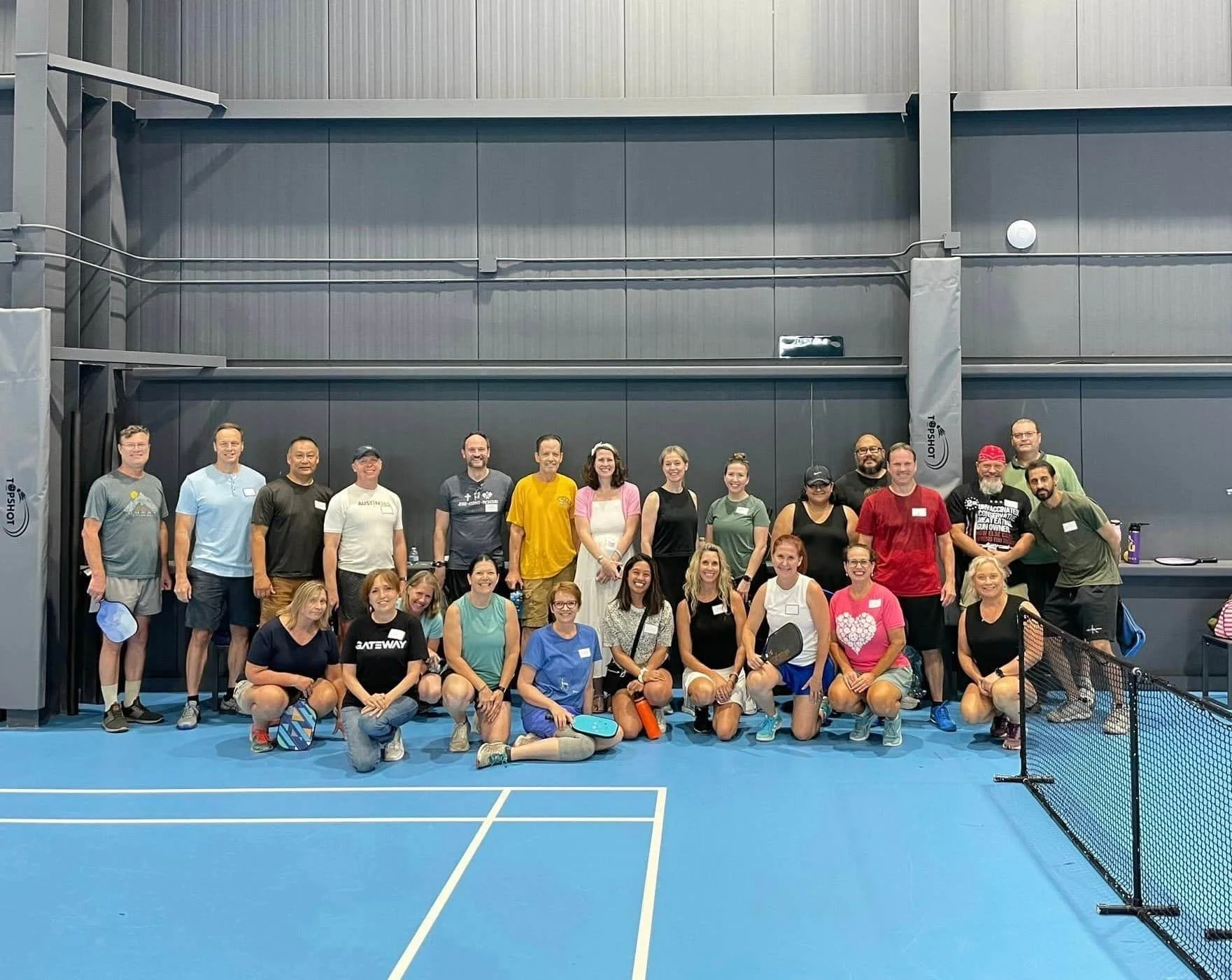A group of people gathered together on an indoor tennis court, posing for a photo.