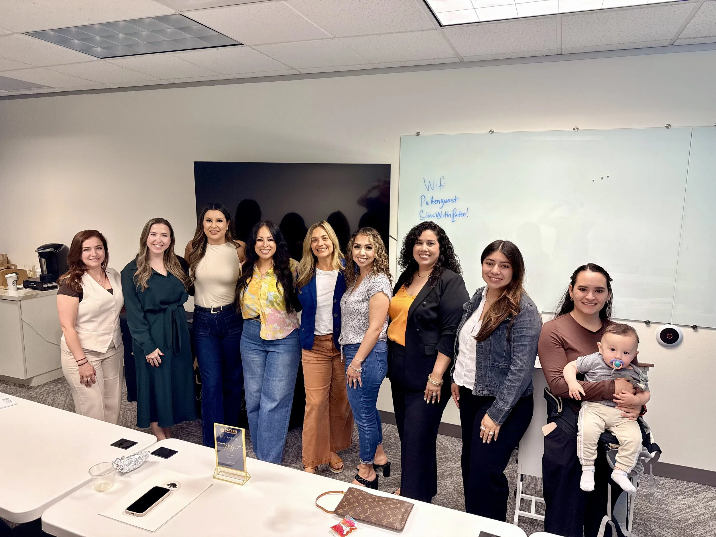 Group of ten women and one child standing in a conference room, smiling at the camera.