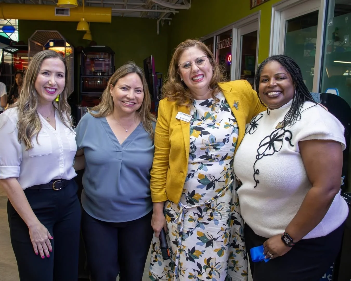 Four women standing together indoors, smiling for the camera.