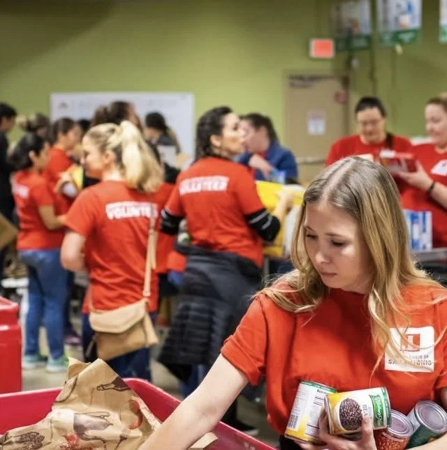A group of volunteers wearing red shirts working together in a community kitchen or food distribution center with a young woman in the foreground sorting food items.