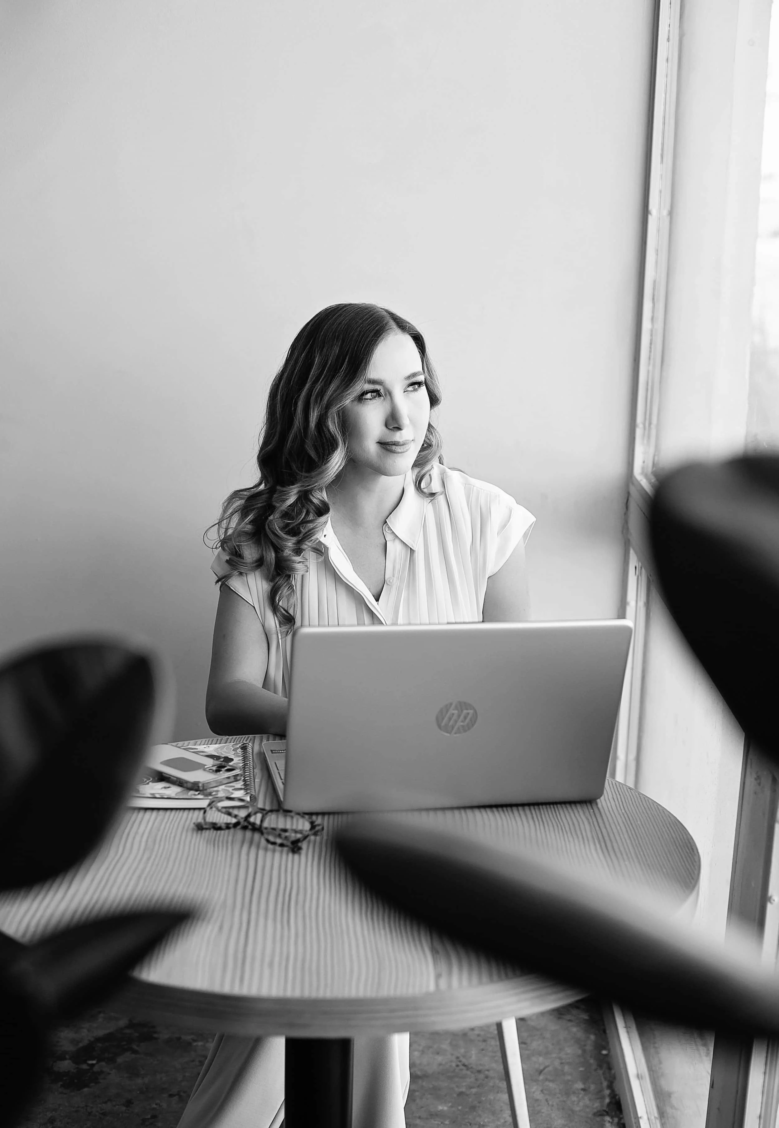 April Guerra, a woman with wavy hair working on a laptop at a round table in a bright room.