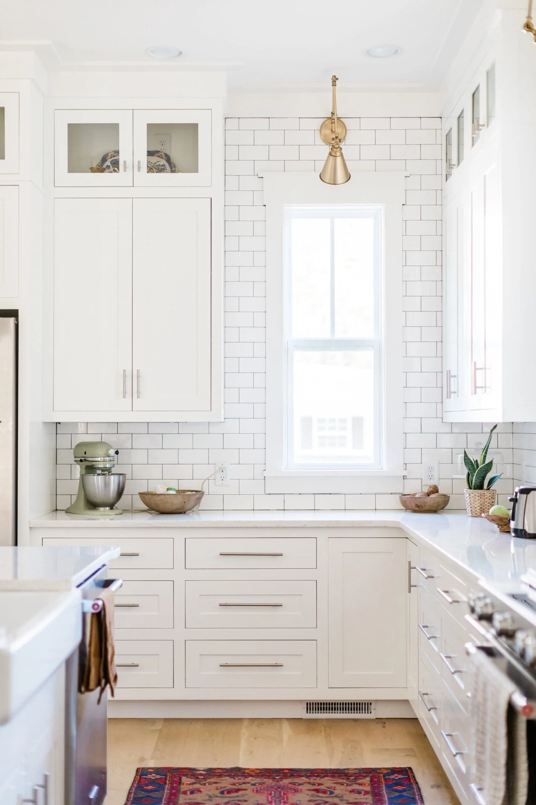 Bright, airy white kitchen with gold fixtures, natural wood accents, large island with seating, and pendant lighting.