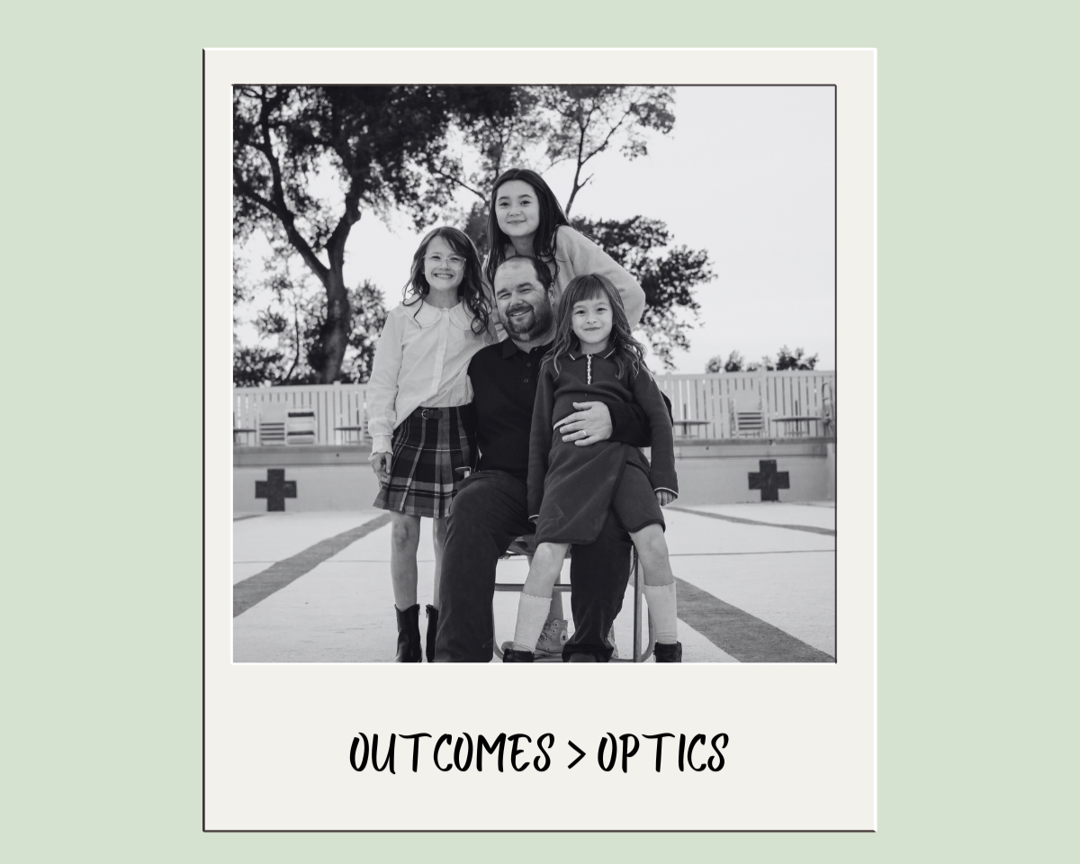 A black and white photo of a man with three young girls outdoors, with trees and a fence in the background, and the phrase 'OUTCOMES > OPTICS' below.