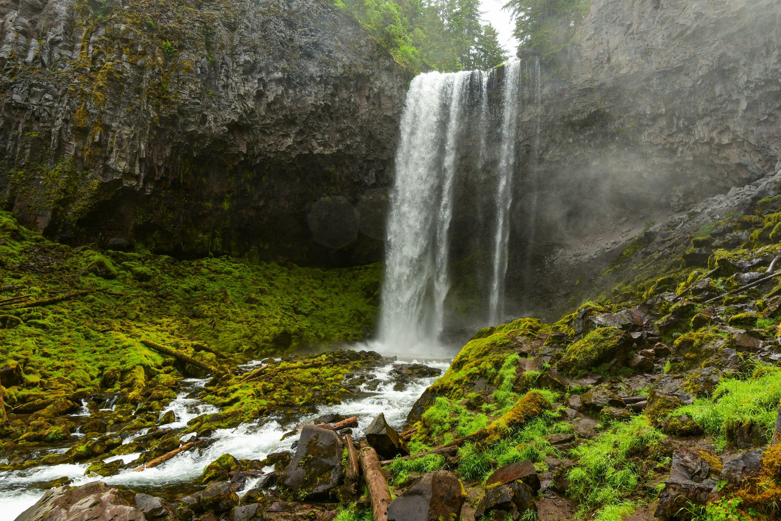 A waterfall cascading over rocky cliffs into a lush, moss-covered landscape with a flowing stream at the bottom.