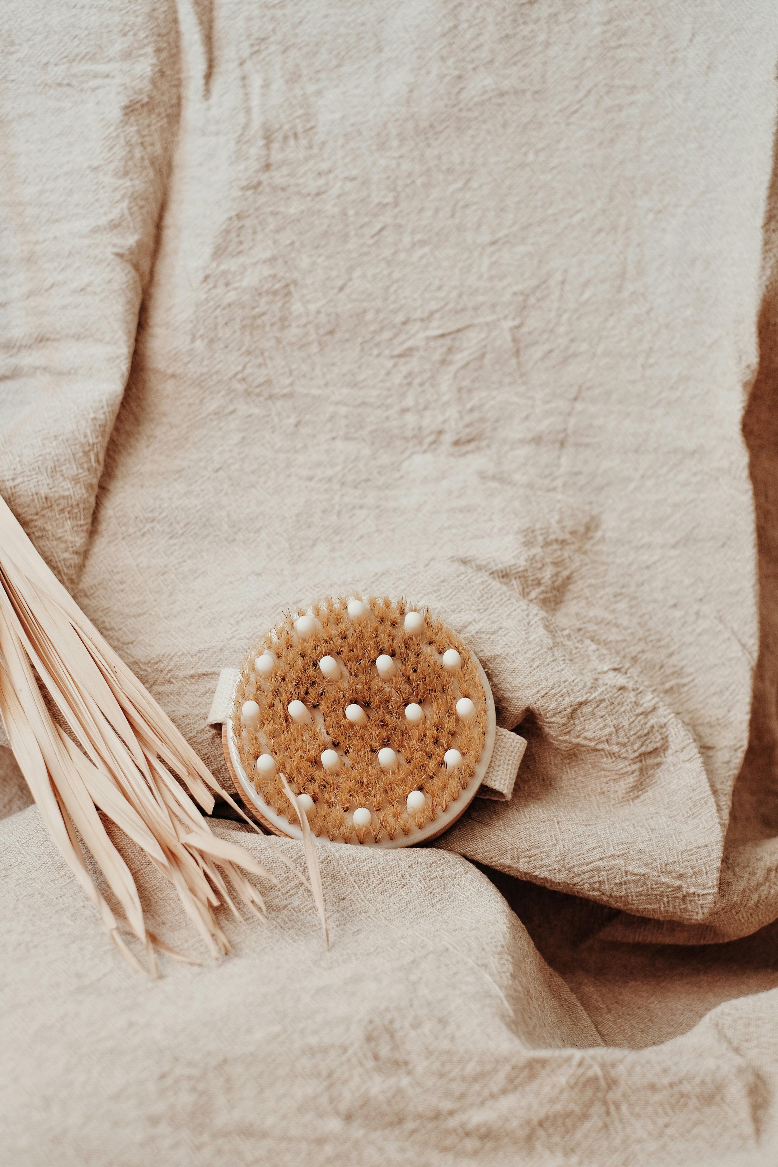 A dry circular brush with white bristles resting on a beige fabric surface, dry brushing available at The Wandering Clay in Oklahoma City