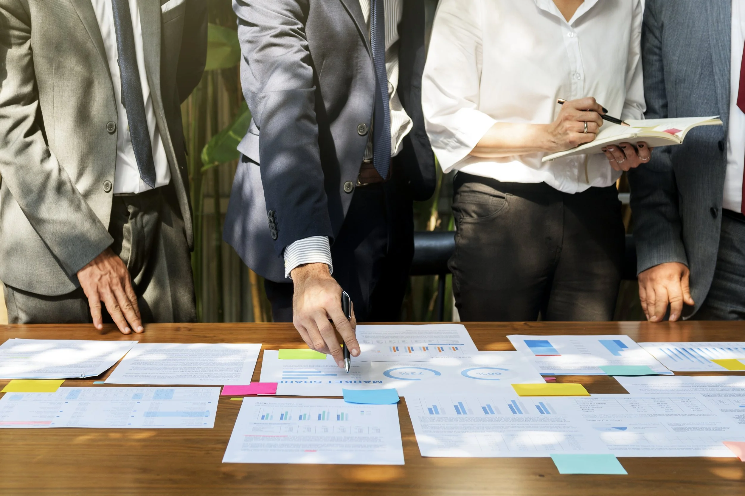 Business professionals reviewing documents and charts on a wooden conference table.