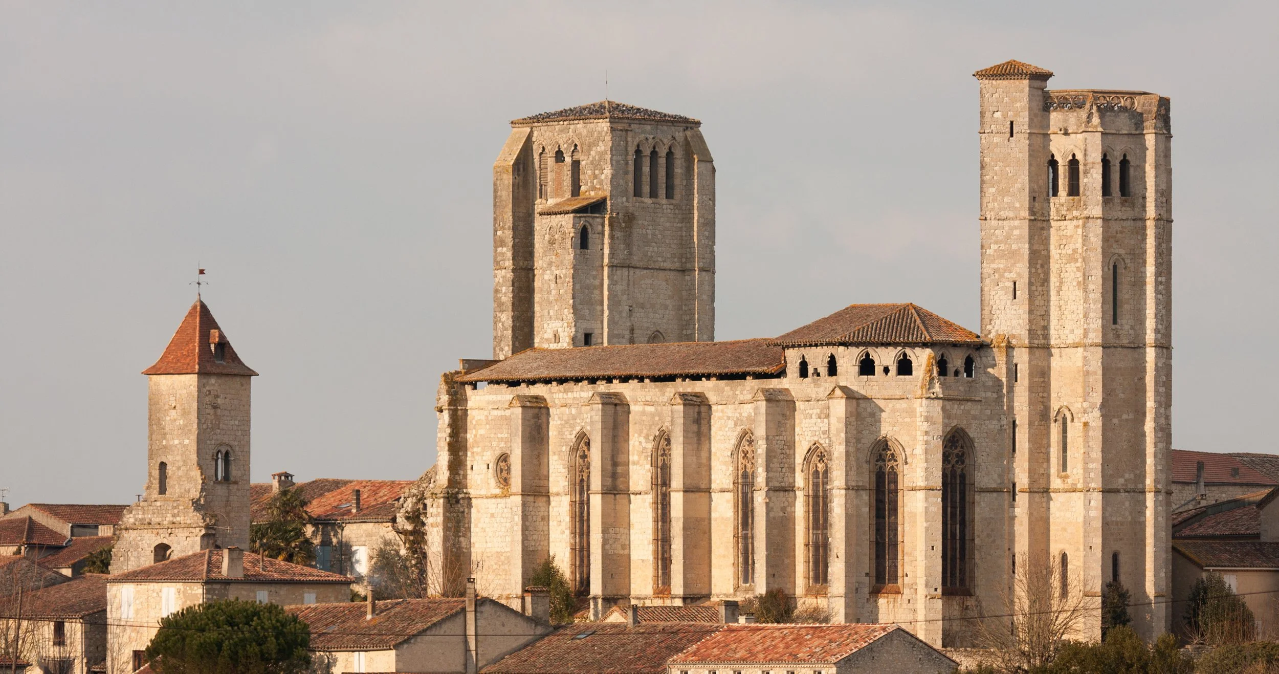 An old stone church with large towers, surrounded by smaller houses with red-tiled roofs.