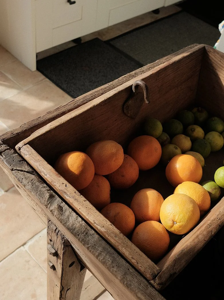 A wooden box on a rustic table containing oranges and green apples.