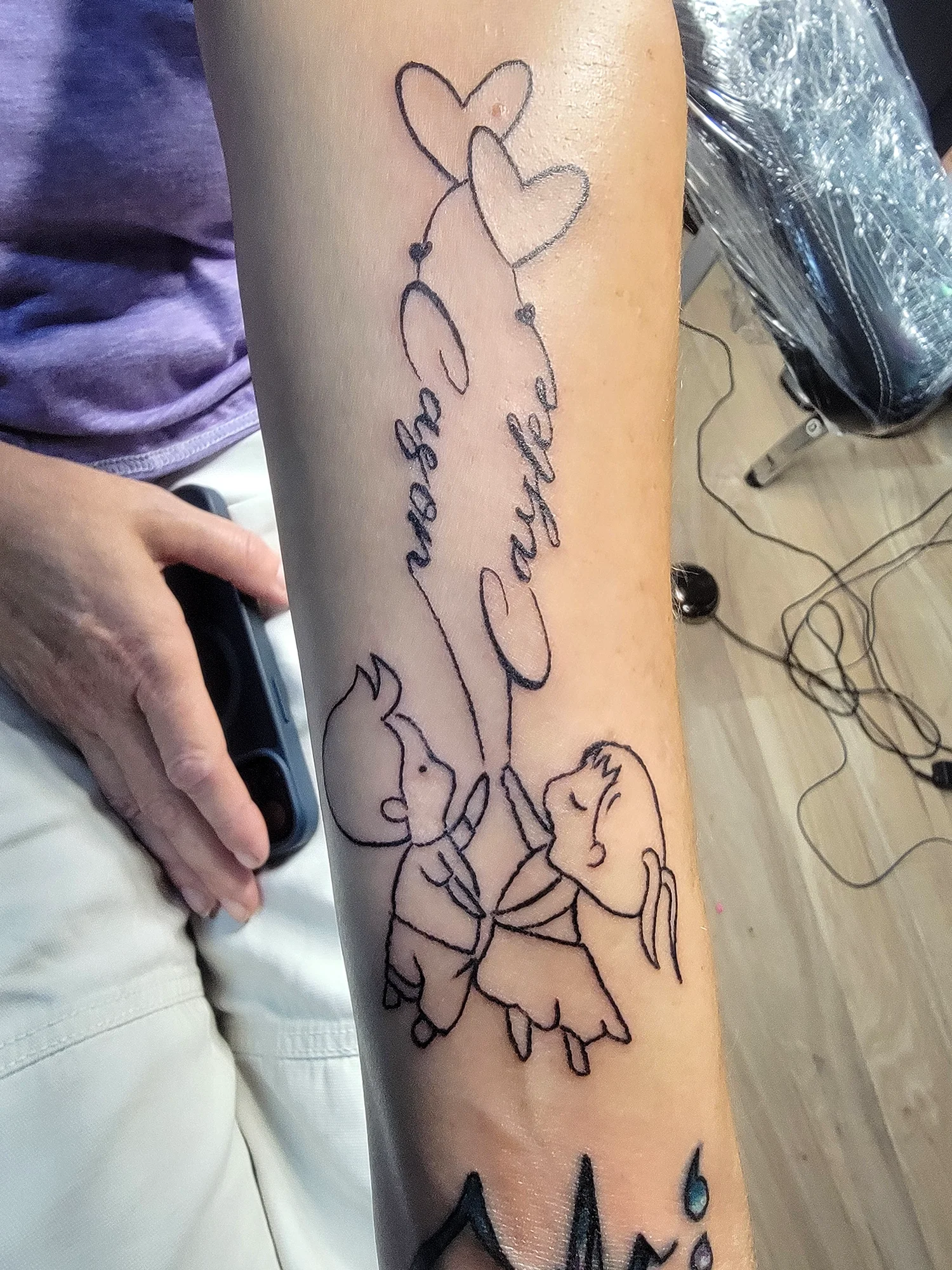 A tattoo of a cartoon monkey holding hands with a girl, with two hearts and the words "The best of" written above.