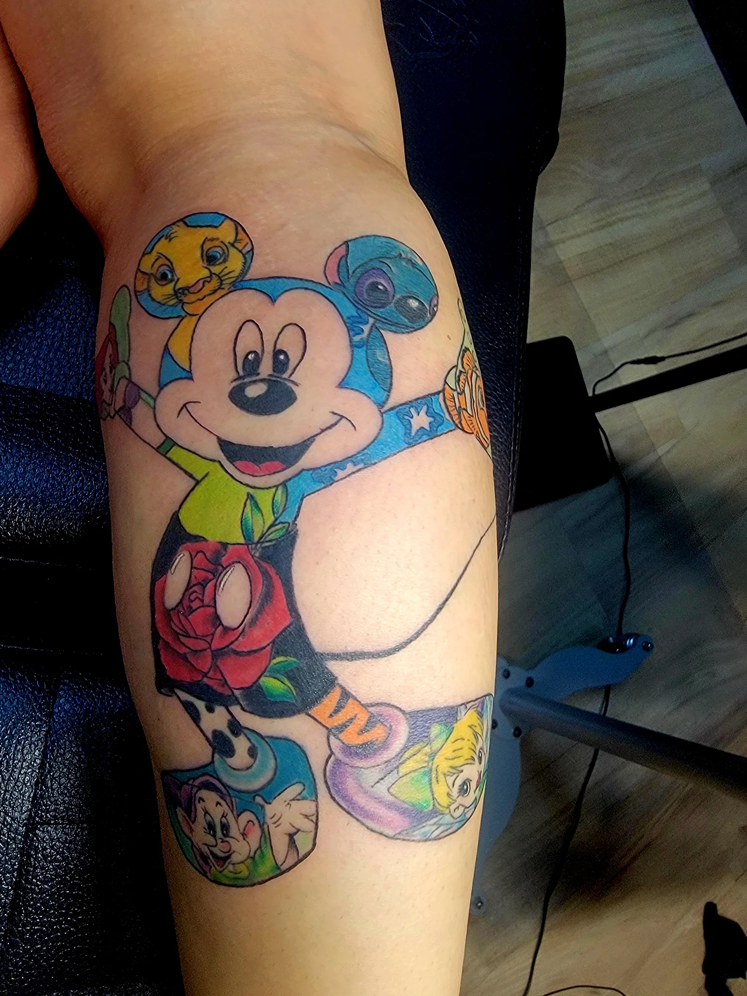 A colorful tattoo sleeve featuring Disney characters Mickey Mouse, Chip and Dale, and others on a person's arm.