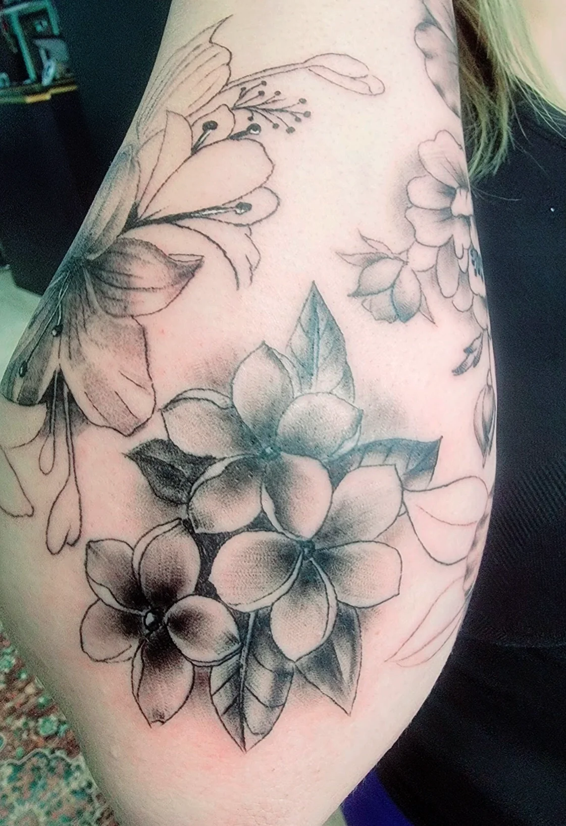 A black and gray floral tattoo on a person's arm featuring large flowers with petals, leaves, and delicate line work.