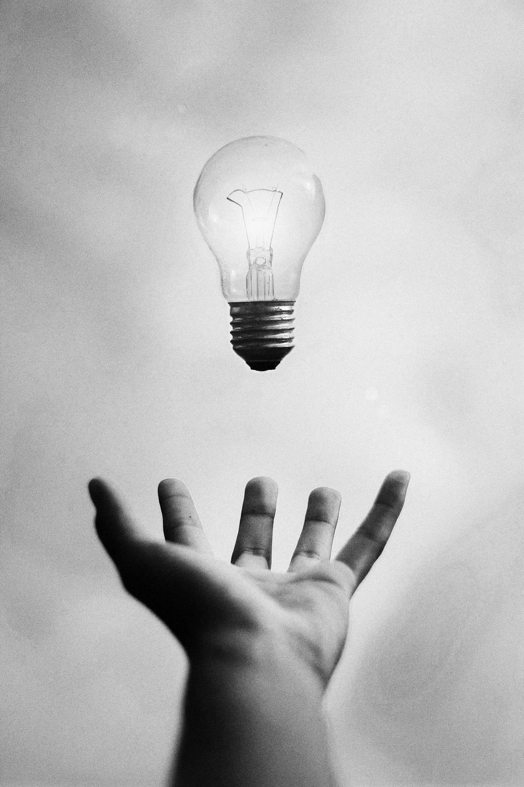 Mano extendida con una bombilla de luz en el aire, en una imagen en escala de grises.