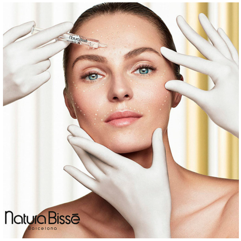 Woman with gloved hands holding her chin and her forehead, in a clinical setting.