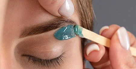 A person applying teal-colored wax using a wooden spatula.