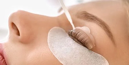 Close-up of a woman receiving an eyelash extension or eyelash treatment with a white pad under the eye.