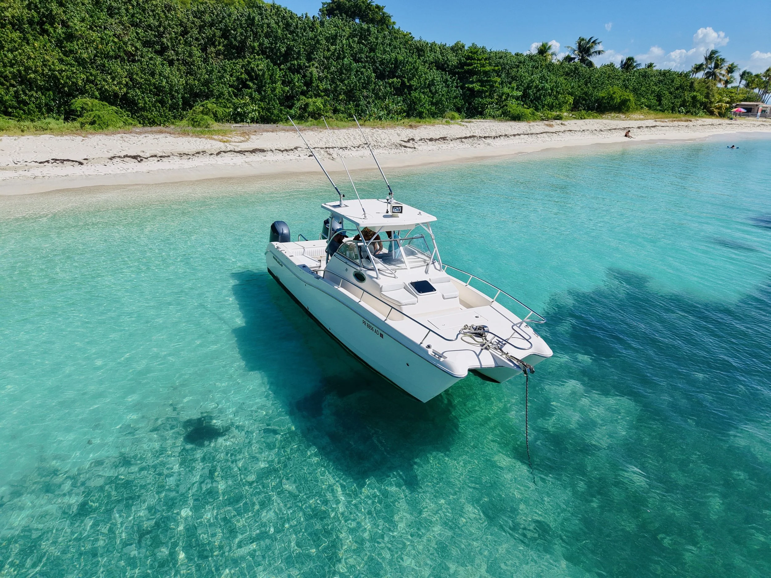 Embarcación de lujo en agua cristalina junto a playa con arena blanca y vegetación tropical.