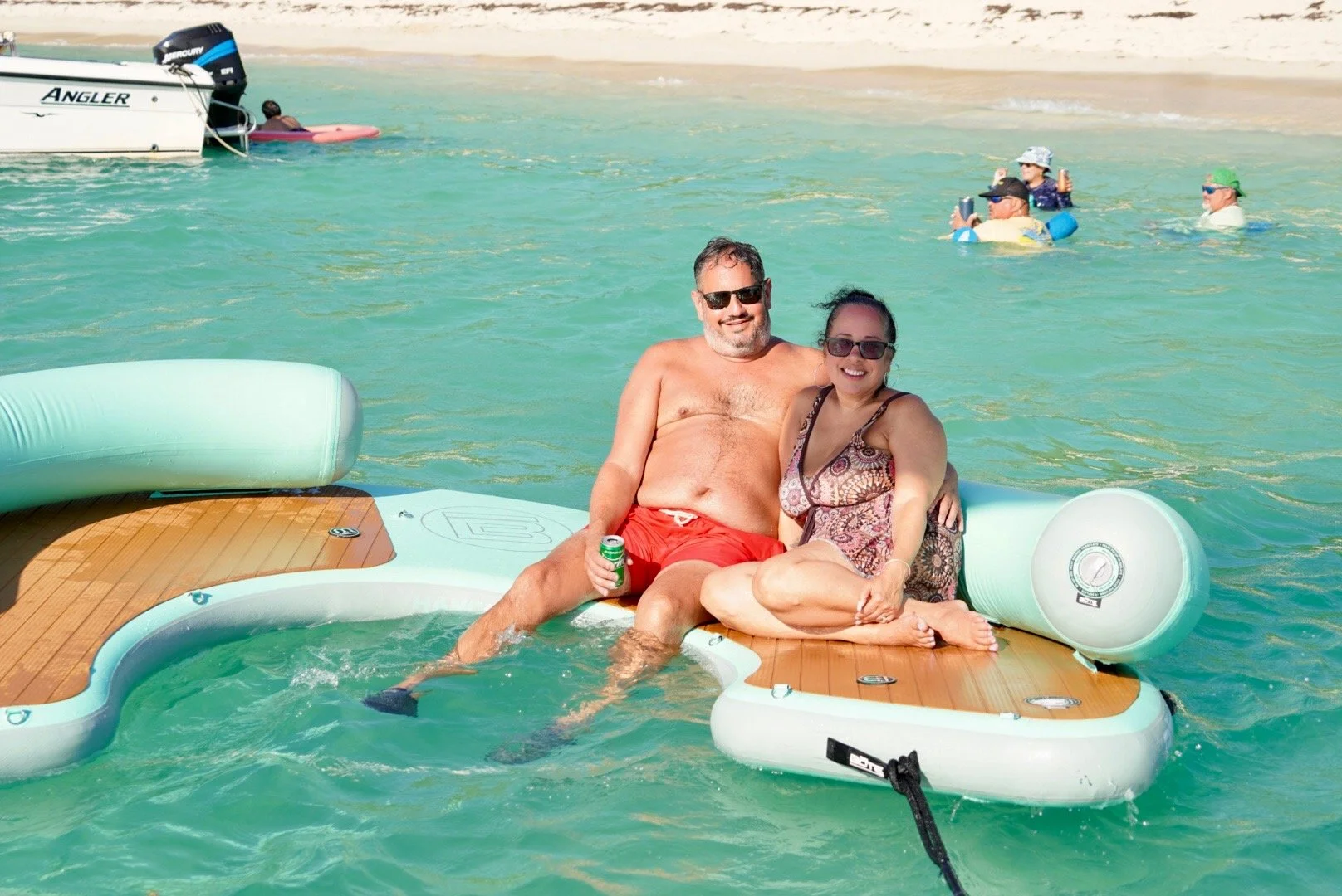 Una pareja disfrutando en una tabla inflable en el agua del mar, rodeada de otras personas en la playa