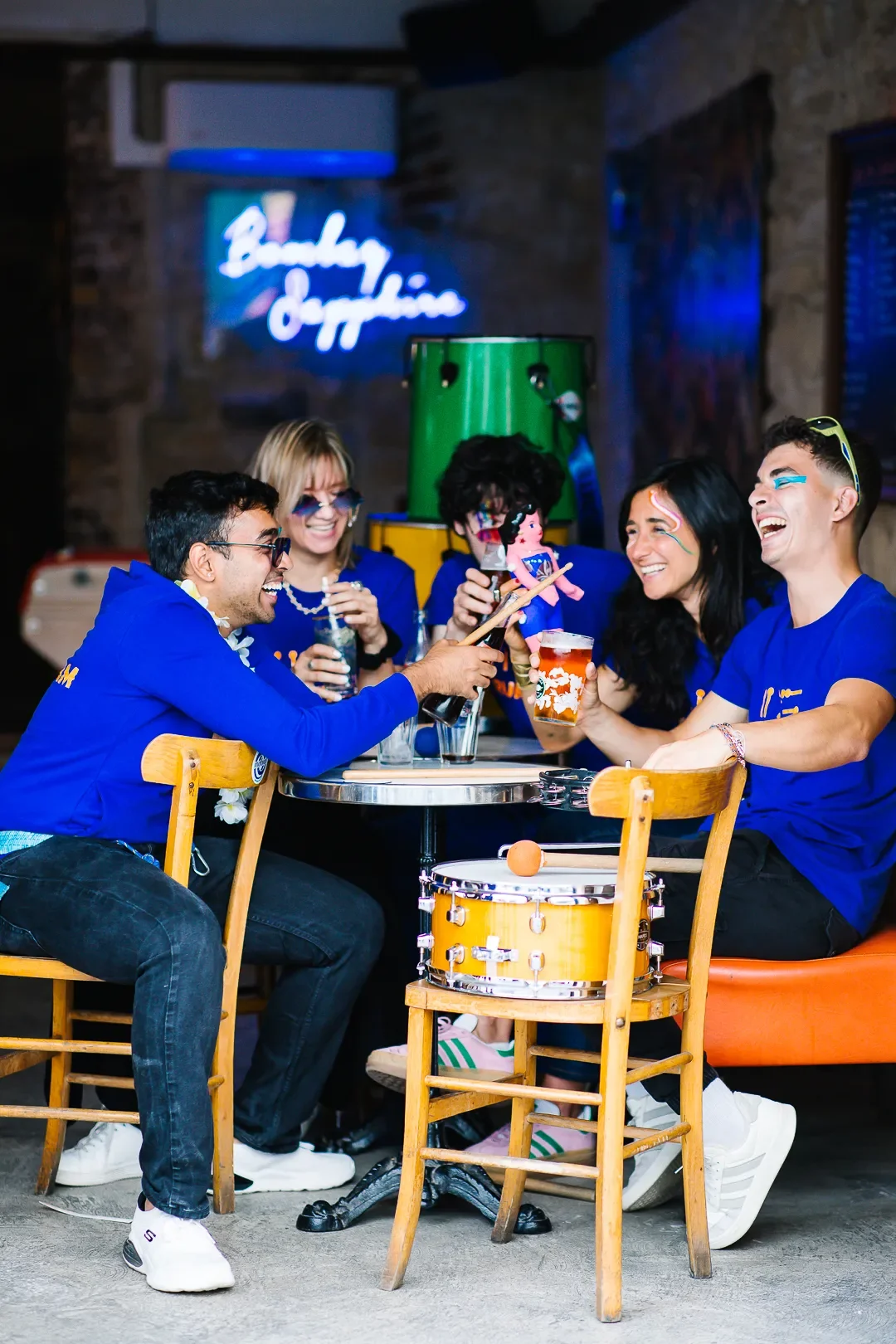 Quatre percussionnistes de la Drumteam photographié·e·s de profil autour d’une table en train de trinquer dans un moment de fête.