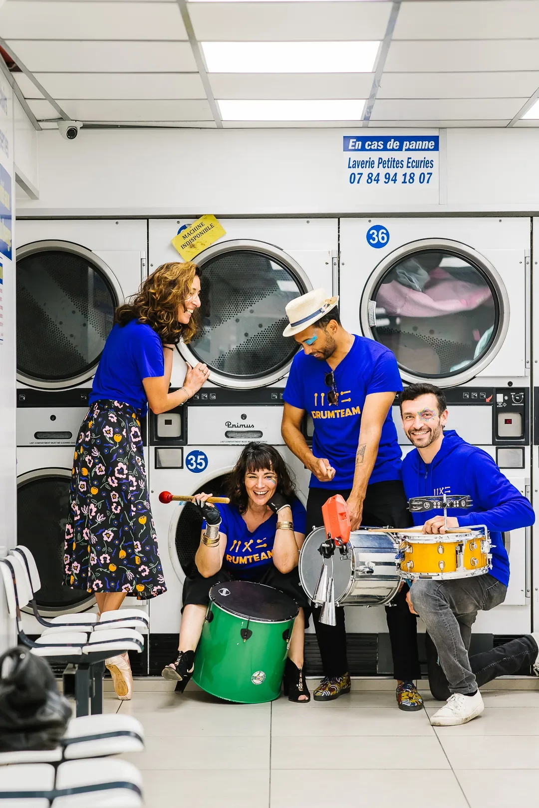 Les membres de la Drumteam posant avec leurs instruments dans une laverie automatique, montrant l'originalité et l'énergie du groupe pour des événements atypiques. Photo : Studio Olympe