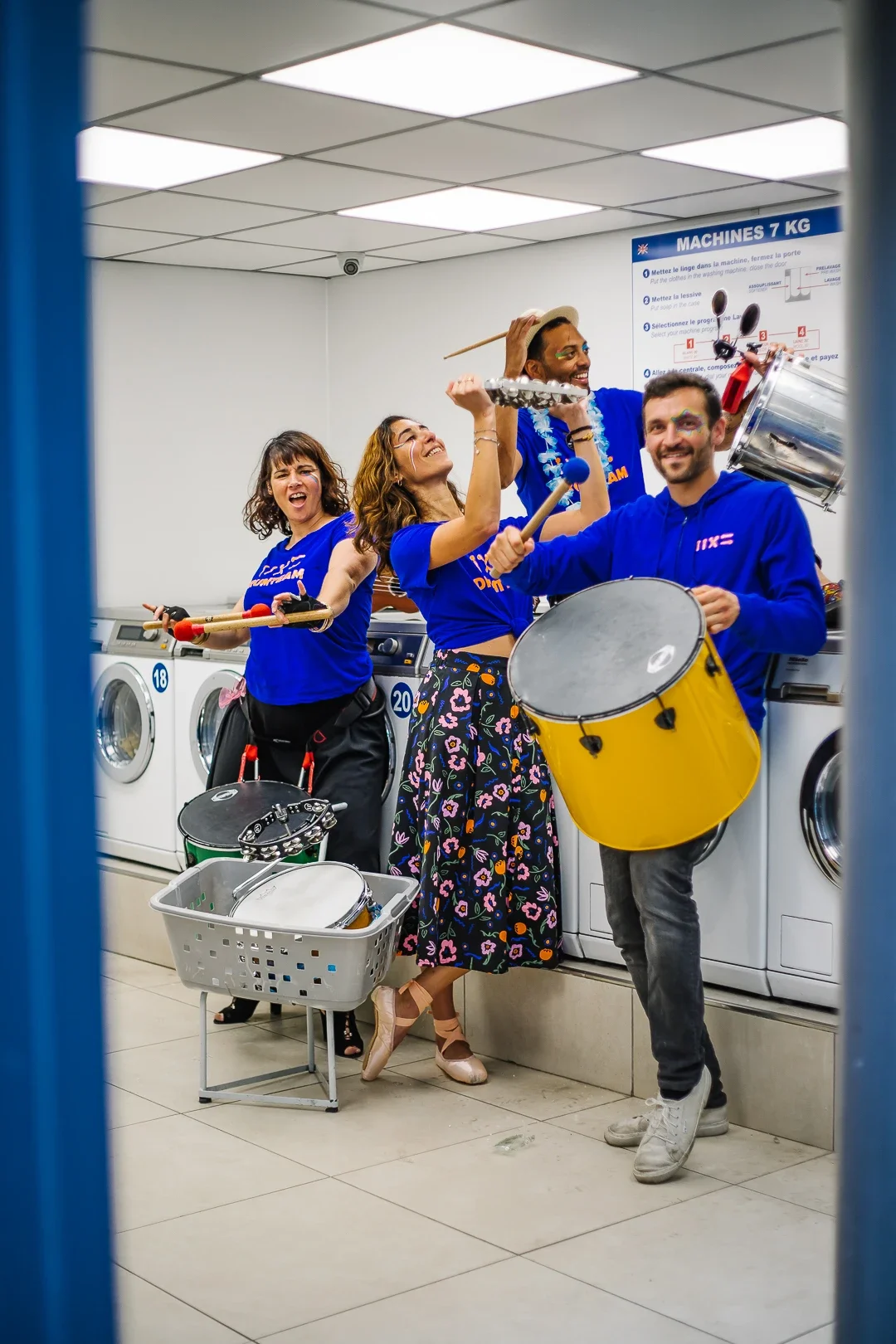 Quatre membres de la Drumteam posant avec enthousiasme et complicité dans le décor insolite d’une laverie automatique à Paris 10. Photo : Studio Olympe