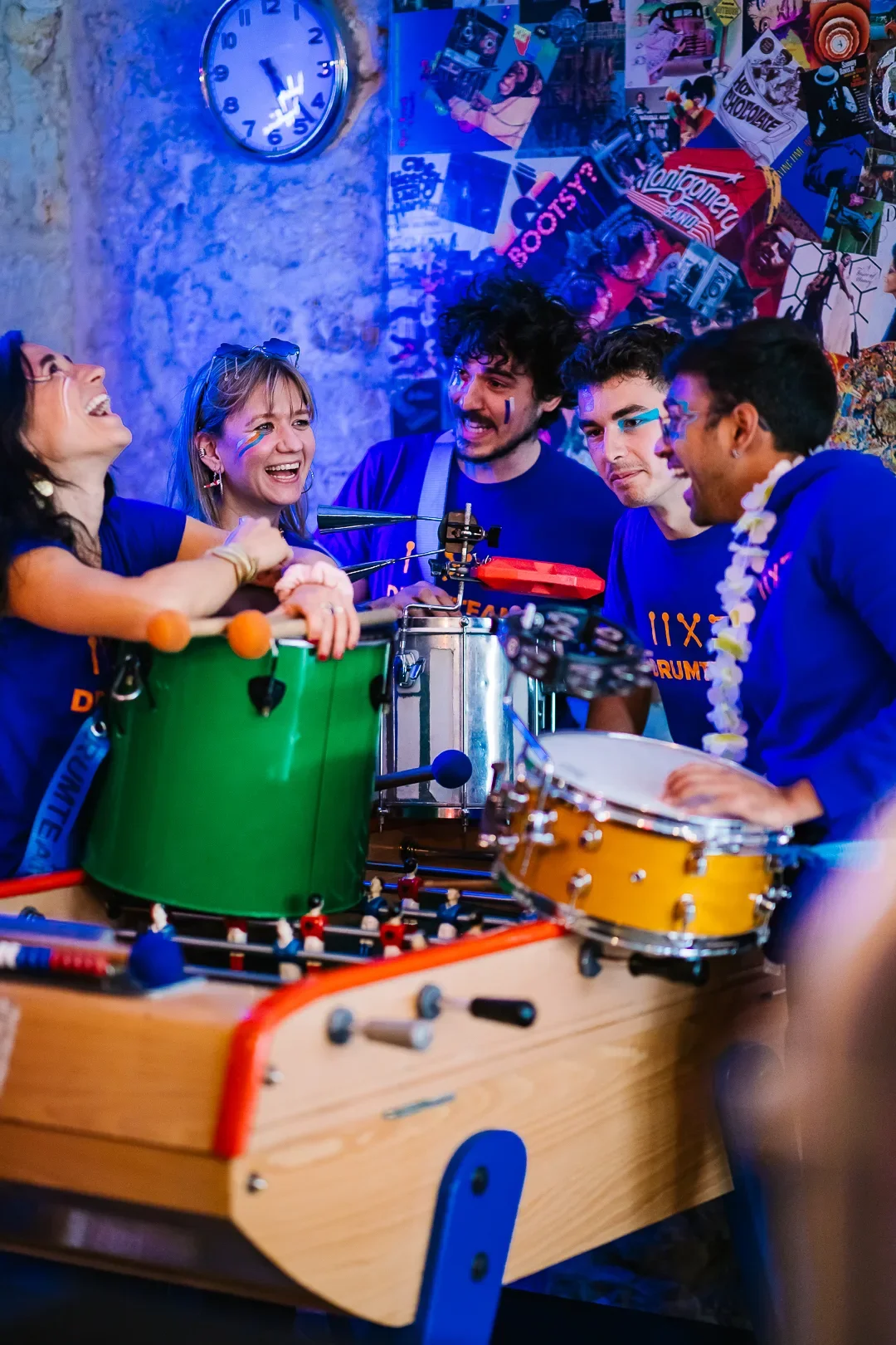 Quatre percussionnistes de la Drumteam photographié·e·s de profil autour d’un babyfoot dans un moment de fête.