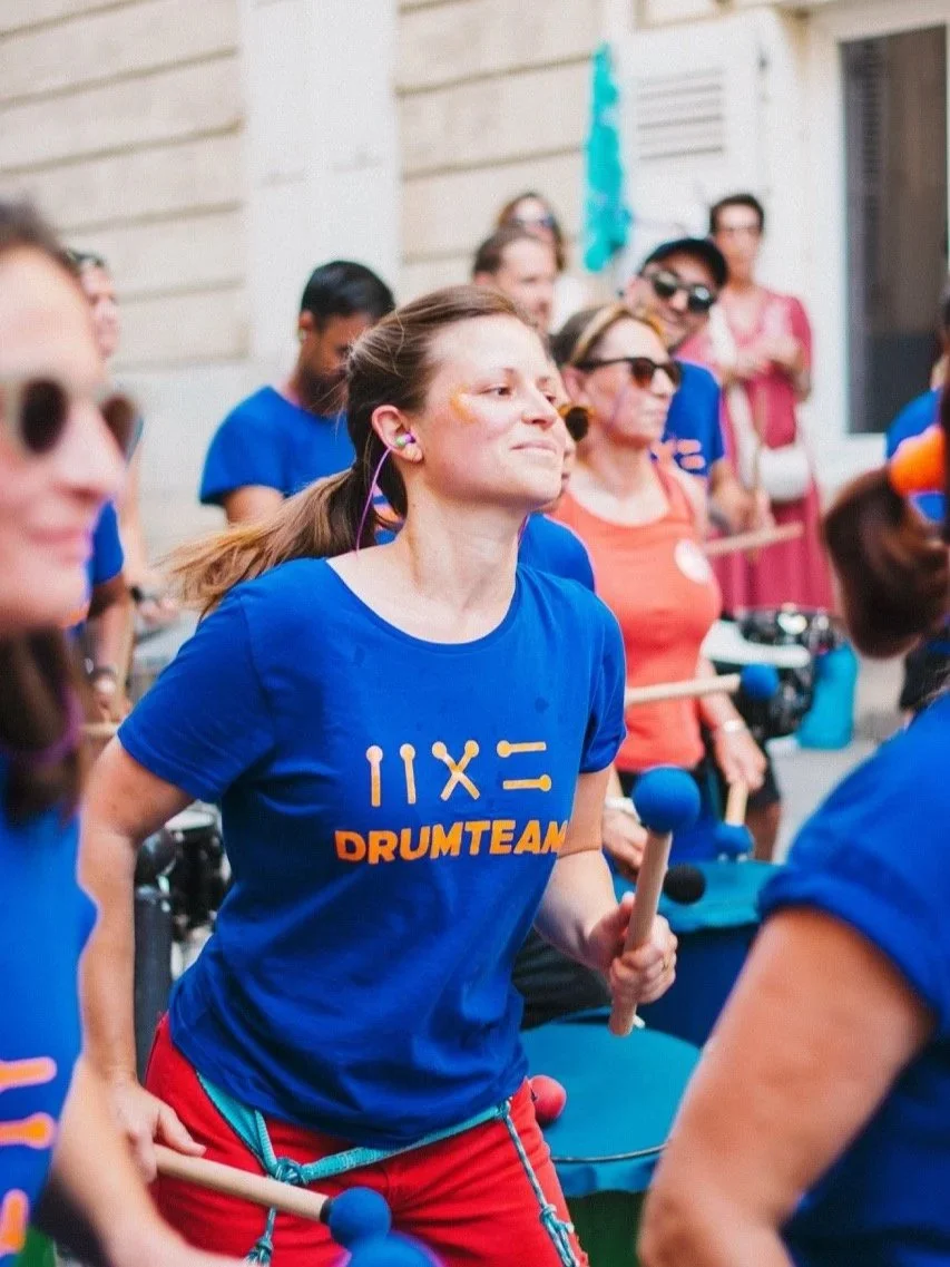 une jeune femme membre de la drumteam paris est en train de jouer entourée d'autres membres à la Fête de la musique 2025