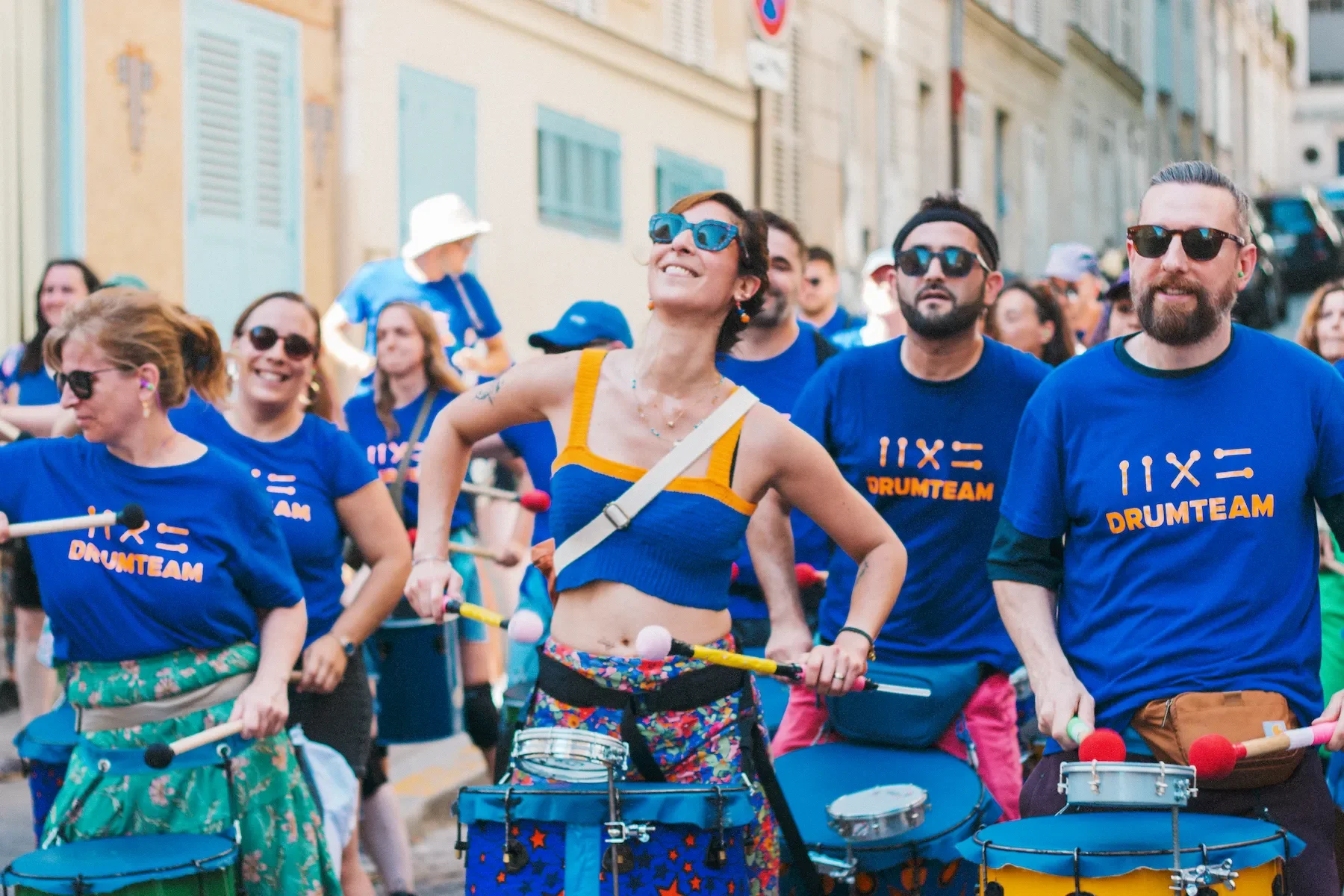 Portrait radieux de membres de la Drumteam défilant dans une rue en pente lors de la Fête de la Musique à Paris. Photo : Studio Olympe