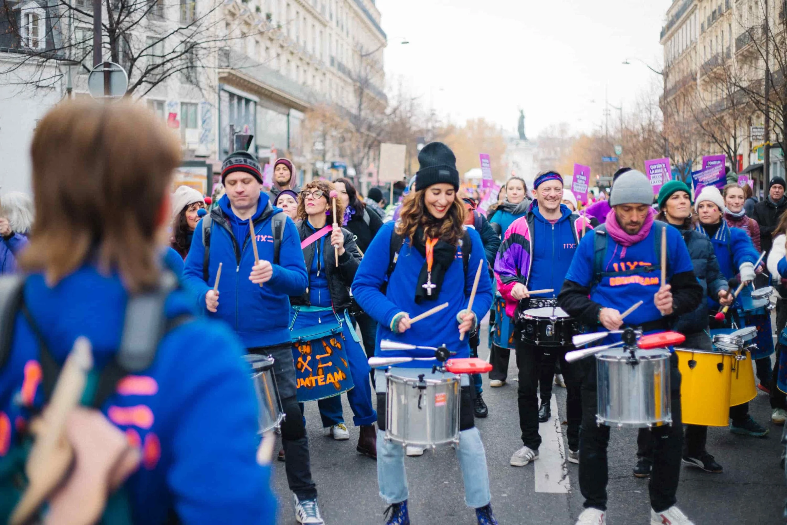 Les membres de la Drumteam défilent avec détermination lors d'une marche féministe à Paris, portant leurs instruments sous un ciel d'hiver. Photo : Studio Olympe