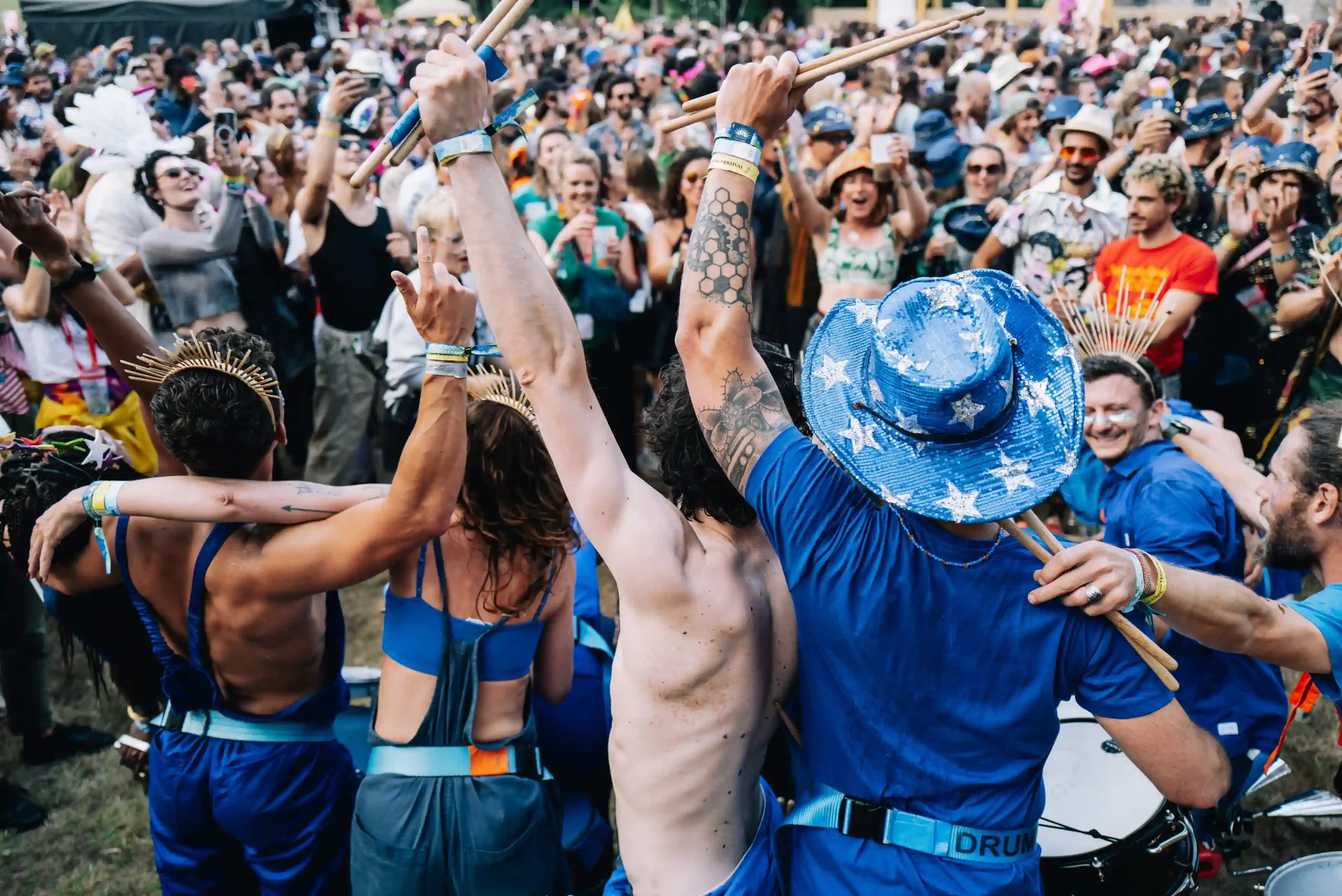 Vue de dos de membres de la Drumteam soudé·e·s, bras dessus bras dessous, face à l'immense foule festive du festival Pete the Monkey. Photo : Antoine Sorel