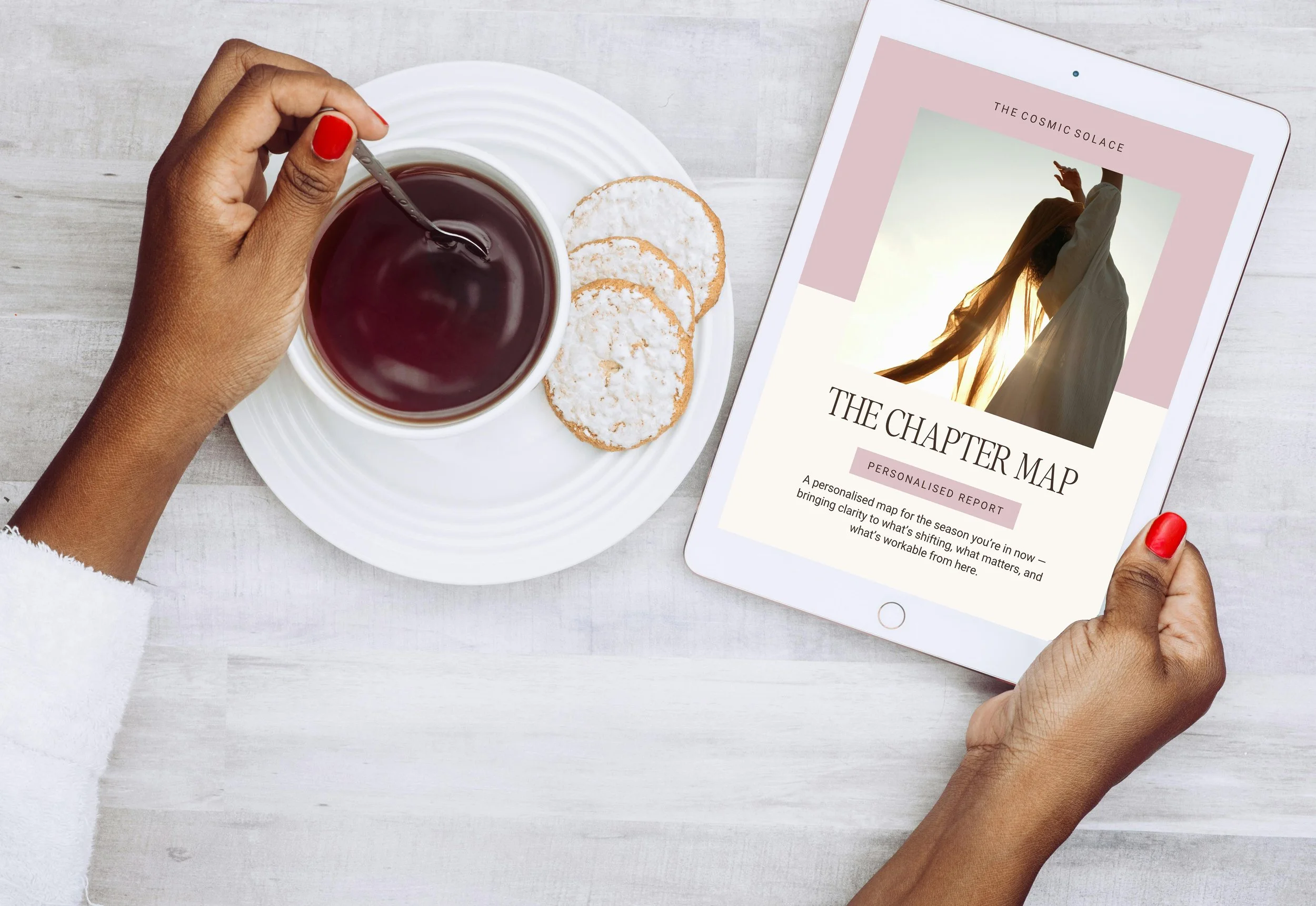 Person holding a tablet with 'The Charter Map' on the screen, next to a cup of tea with three cookies on a white plate, on a light gray wooden table.