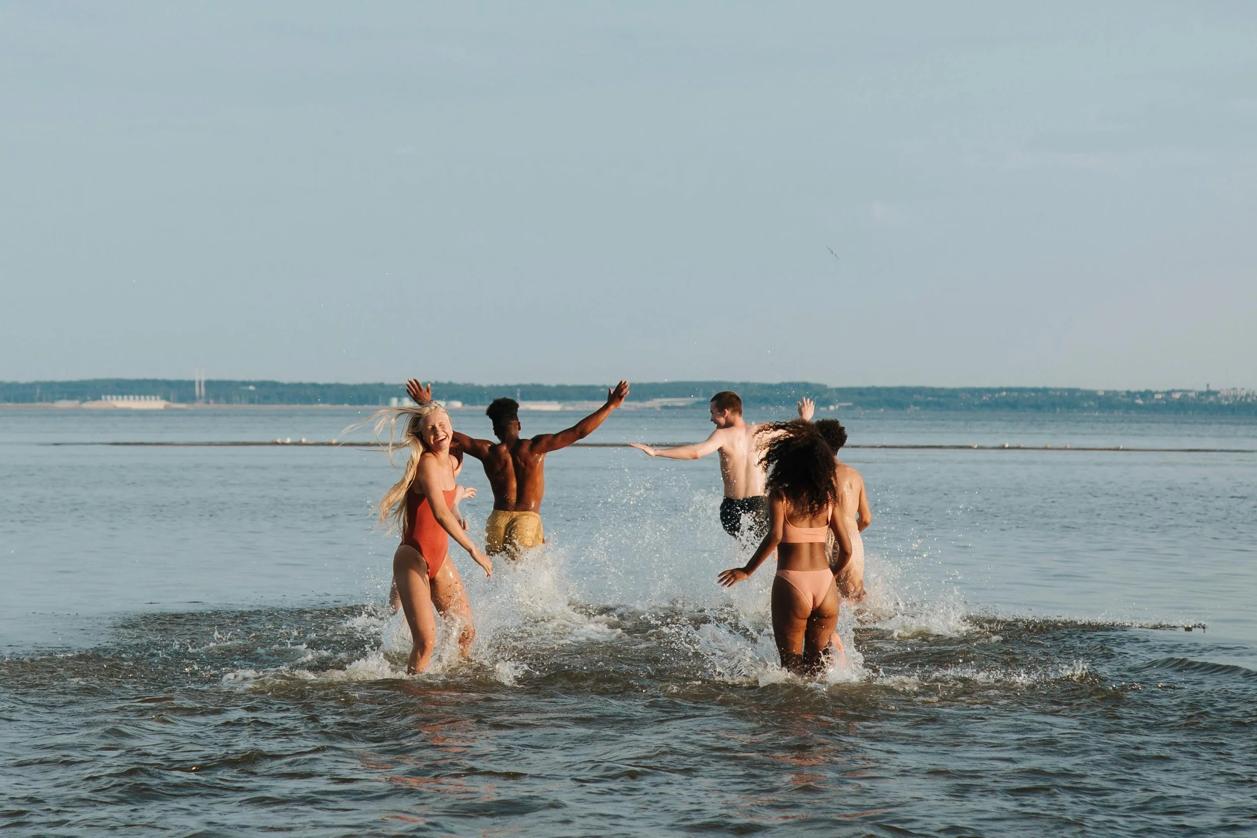 A group of five young people playing and splashing in the water at a beach on a sunny day.