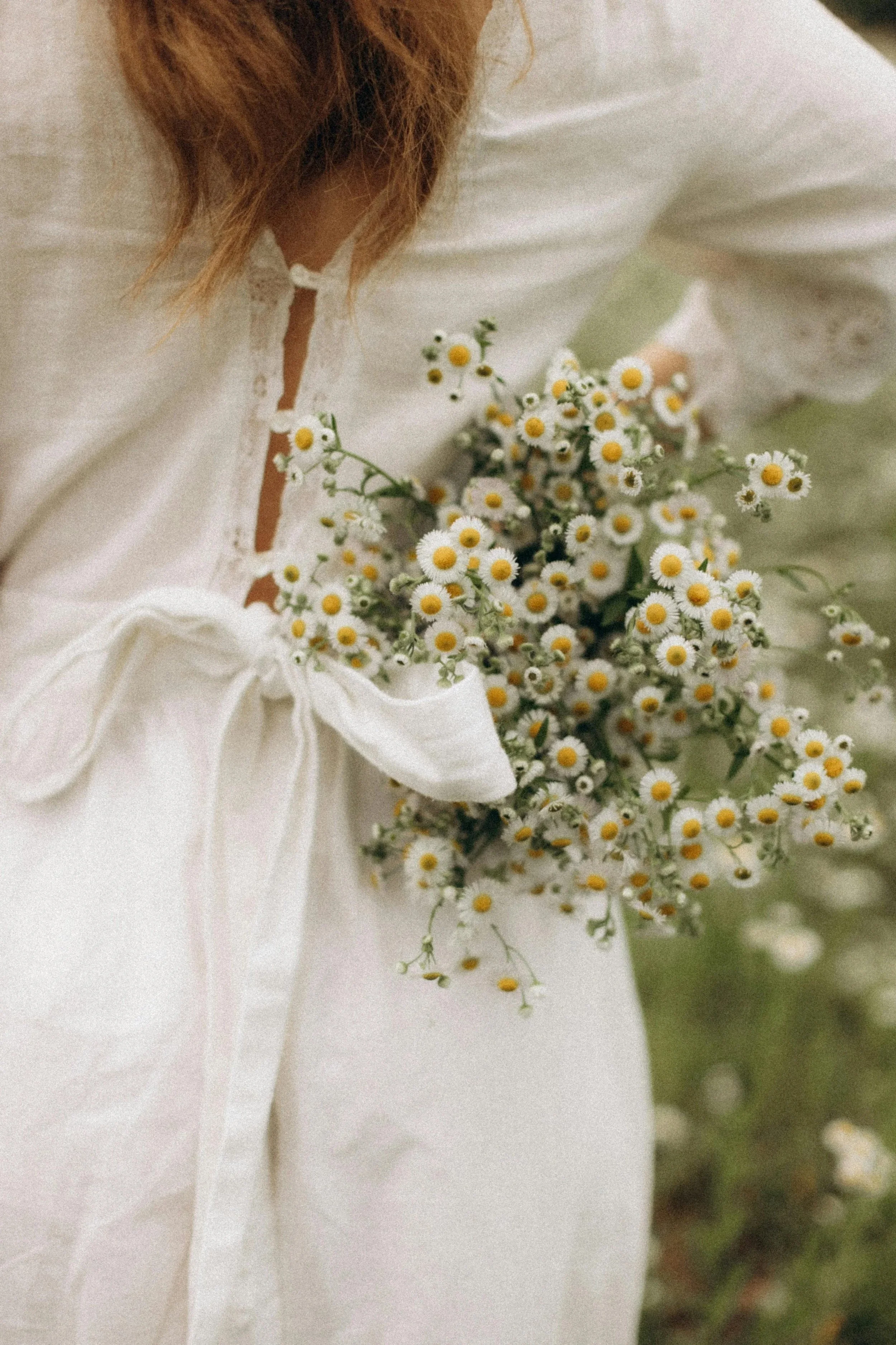 A woman in a white dress with her back facing holding a bouquet of daisies