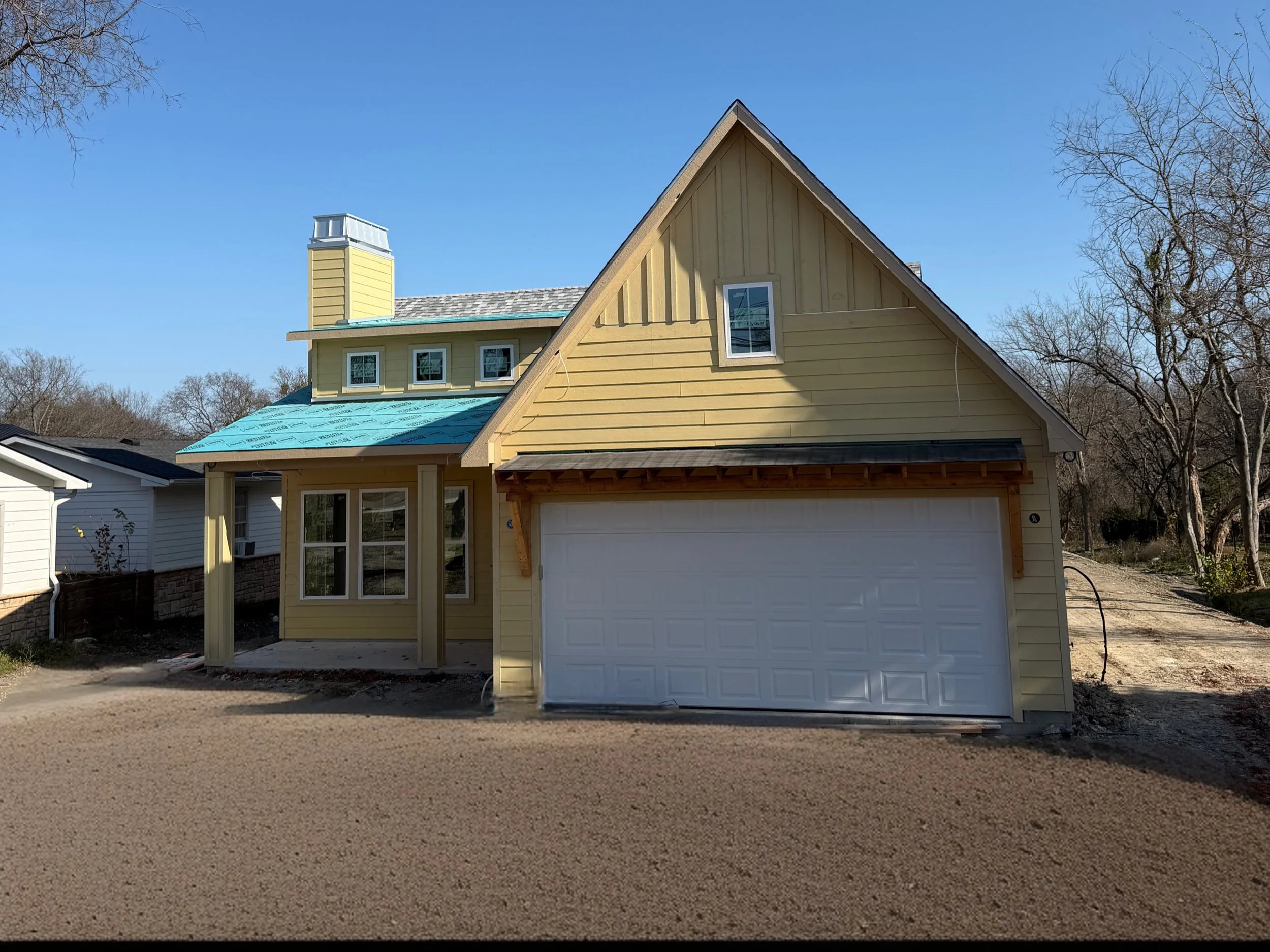 A yellow house under construction with a blue roof in a suburban neighborhood during daytime.