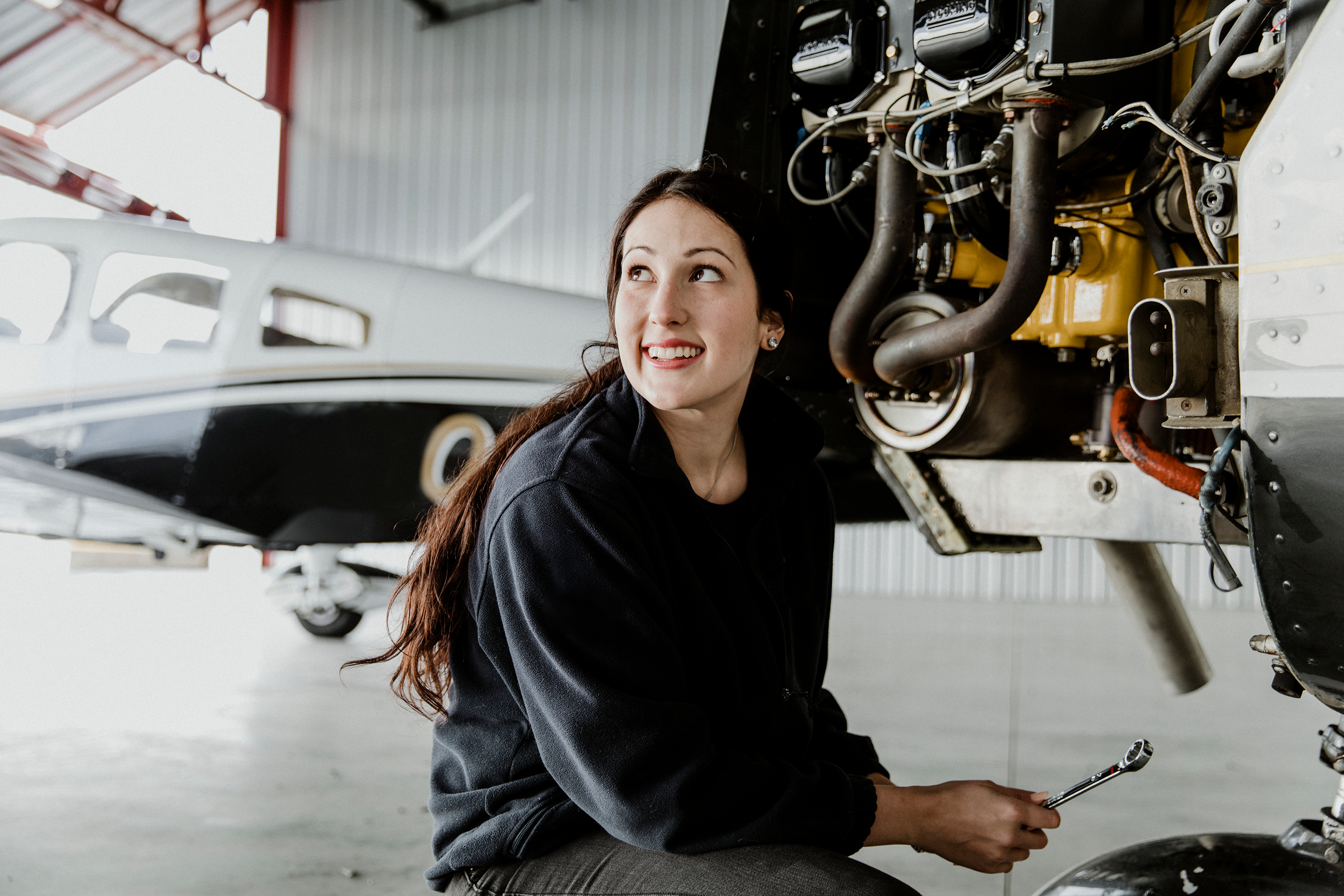 Young woman inspecting an aircraft engine with a wrench inside a hangar.