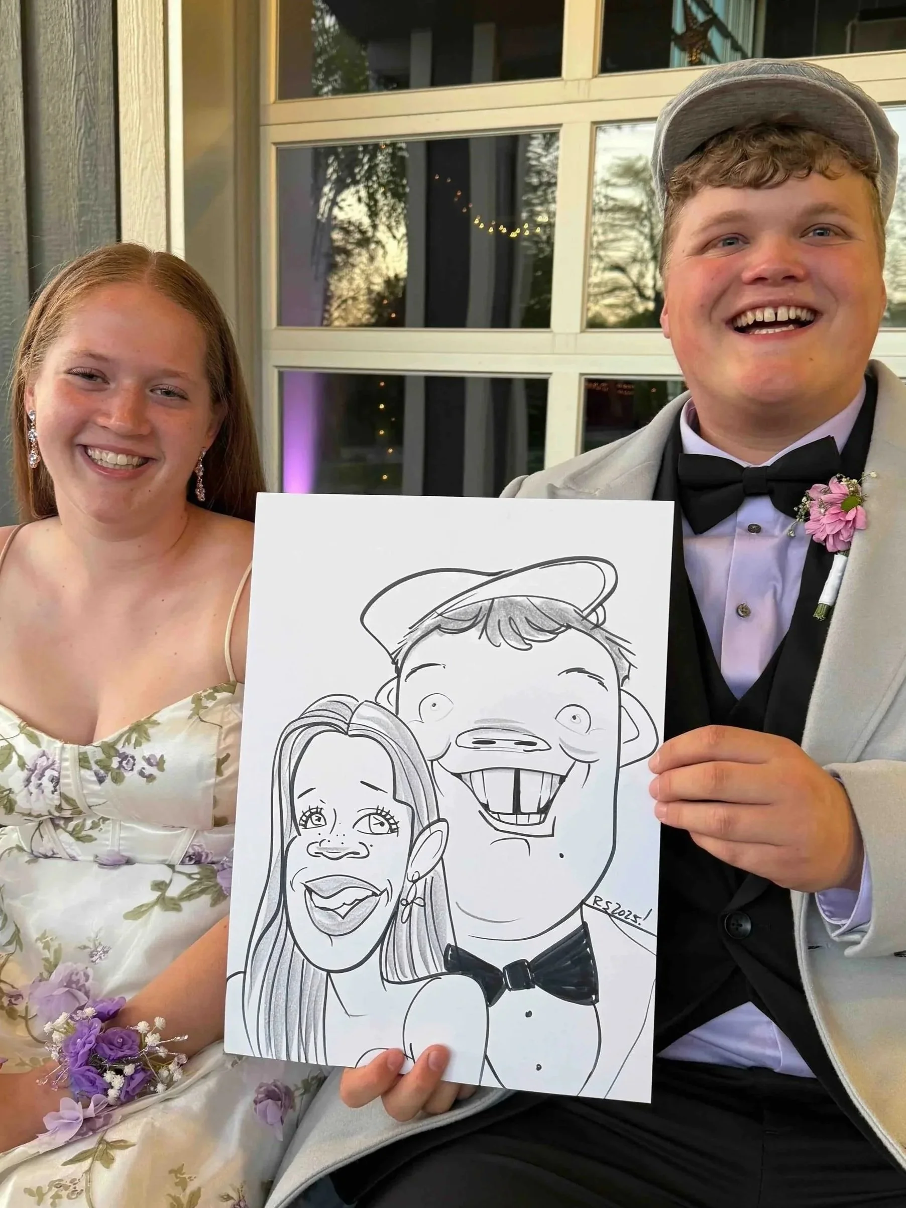 Young man in a tuxedo and woman in a floral dress holding their caricature portrait drawn live at a formal celebration or wedding reception.