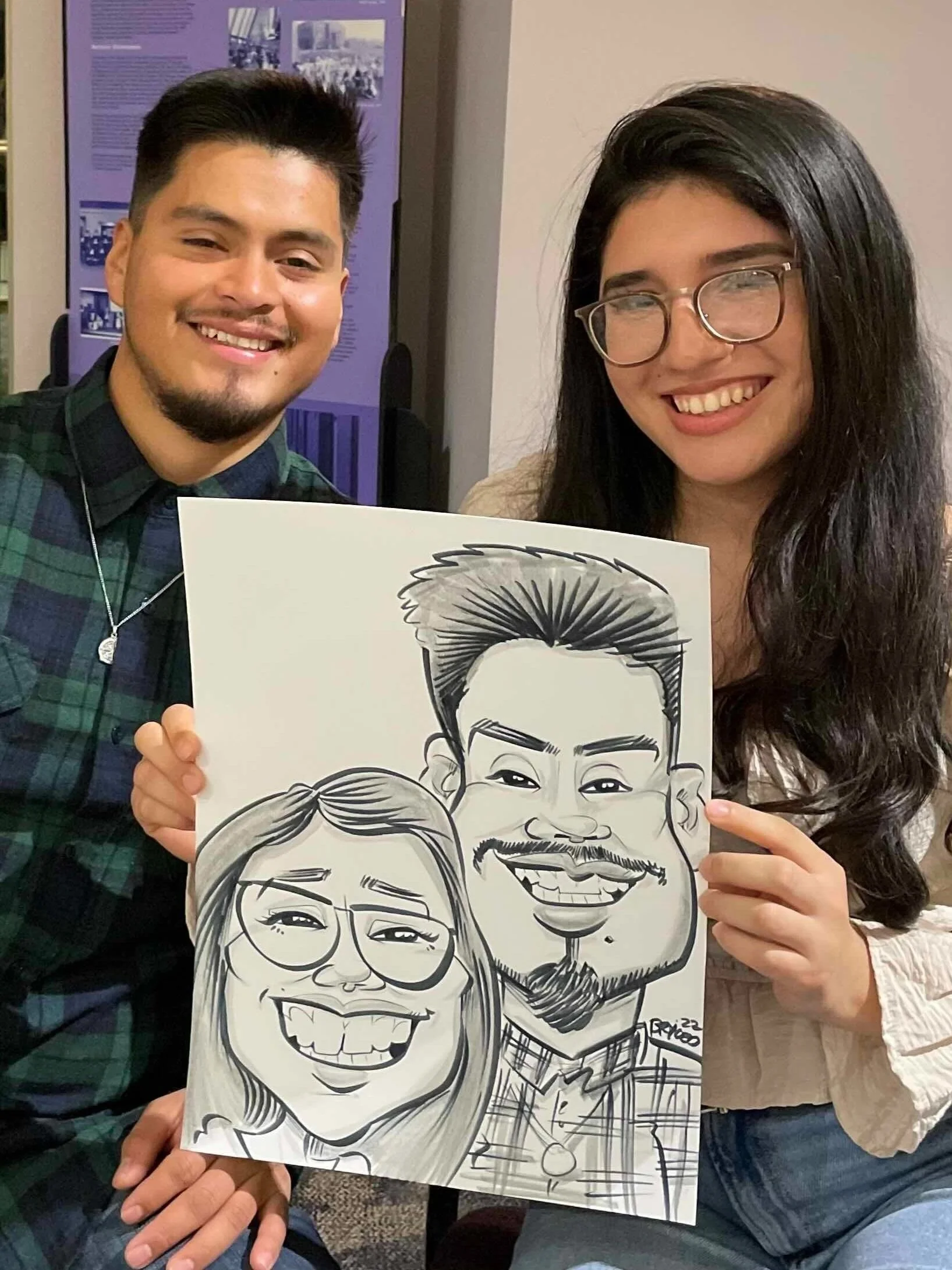 Man and woman holding a caricature drawing of themselves at a Minneapolis event, both smiling for the camera.