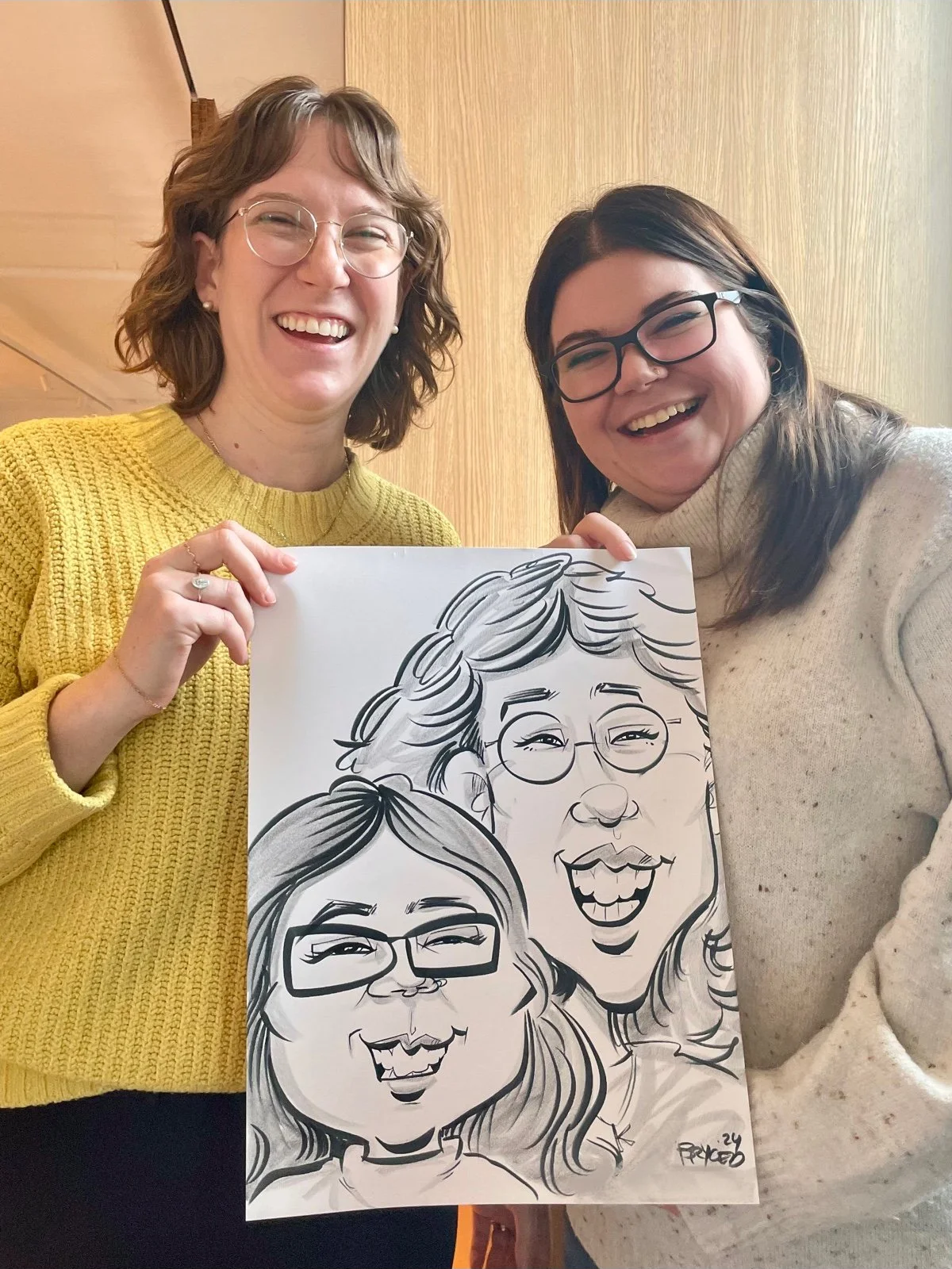 Two women with big smiles holding a black and white caricature of themselves drawn live at a Twin Cities event.