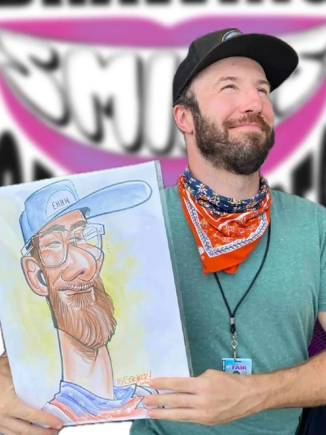 Bearded man in a green shirt and bandana holding his caricature in front of DRAWING SMILES Caricatures banner