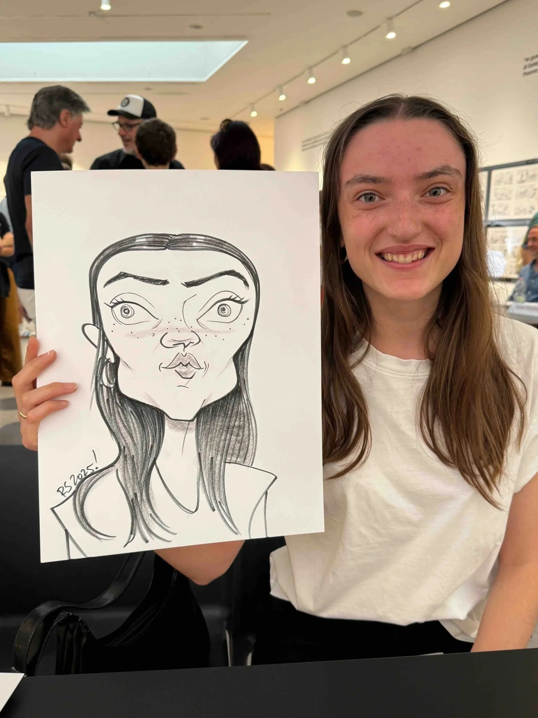 Young woman with long brown hair delighted by her caricature portrait at a gallery event, surrounded by guests in the background.