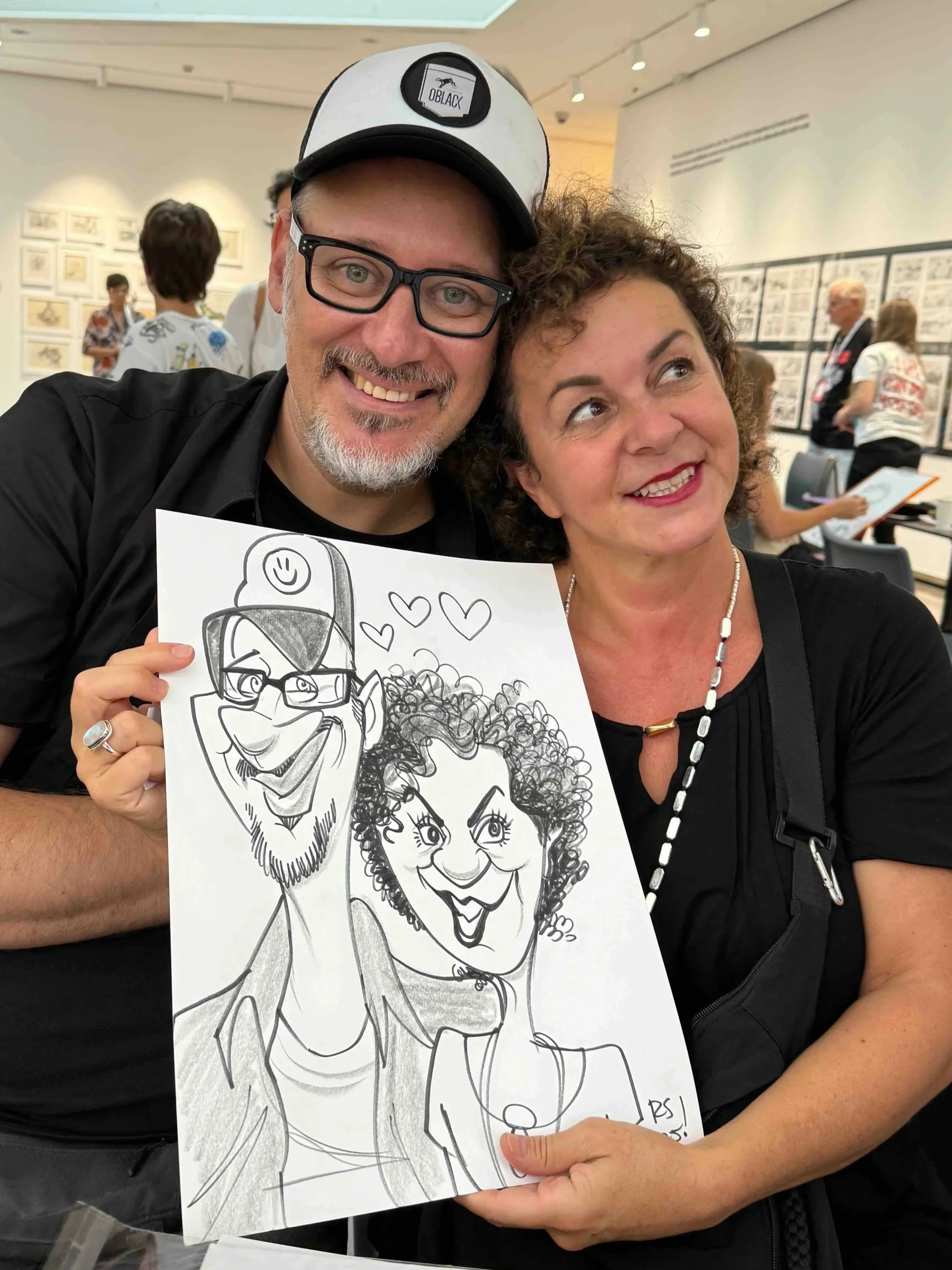 Couple posing with their live caricature drawing at a Minneapolis art and event venue, both grinning at the camera.