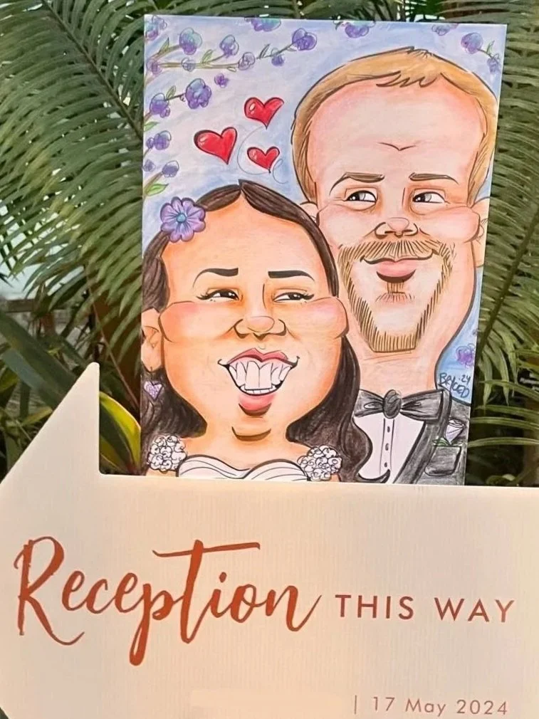 Colorful wedding caricature of a couple in formal attire, displayed near a reception sign reading 'Reception this way'