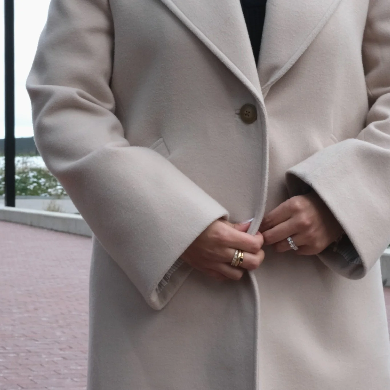 Person buttoning up a cream-colored coat.