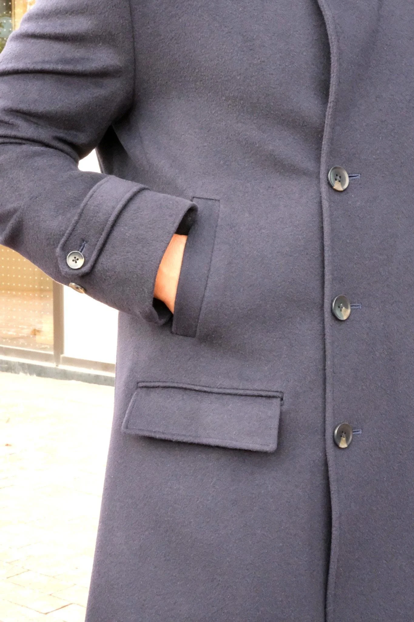 Close-up of a person wearing a dark gray overcoat with one hand in their pocket.