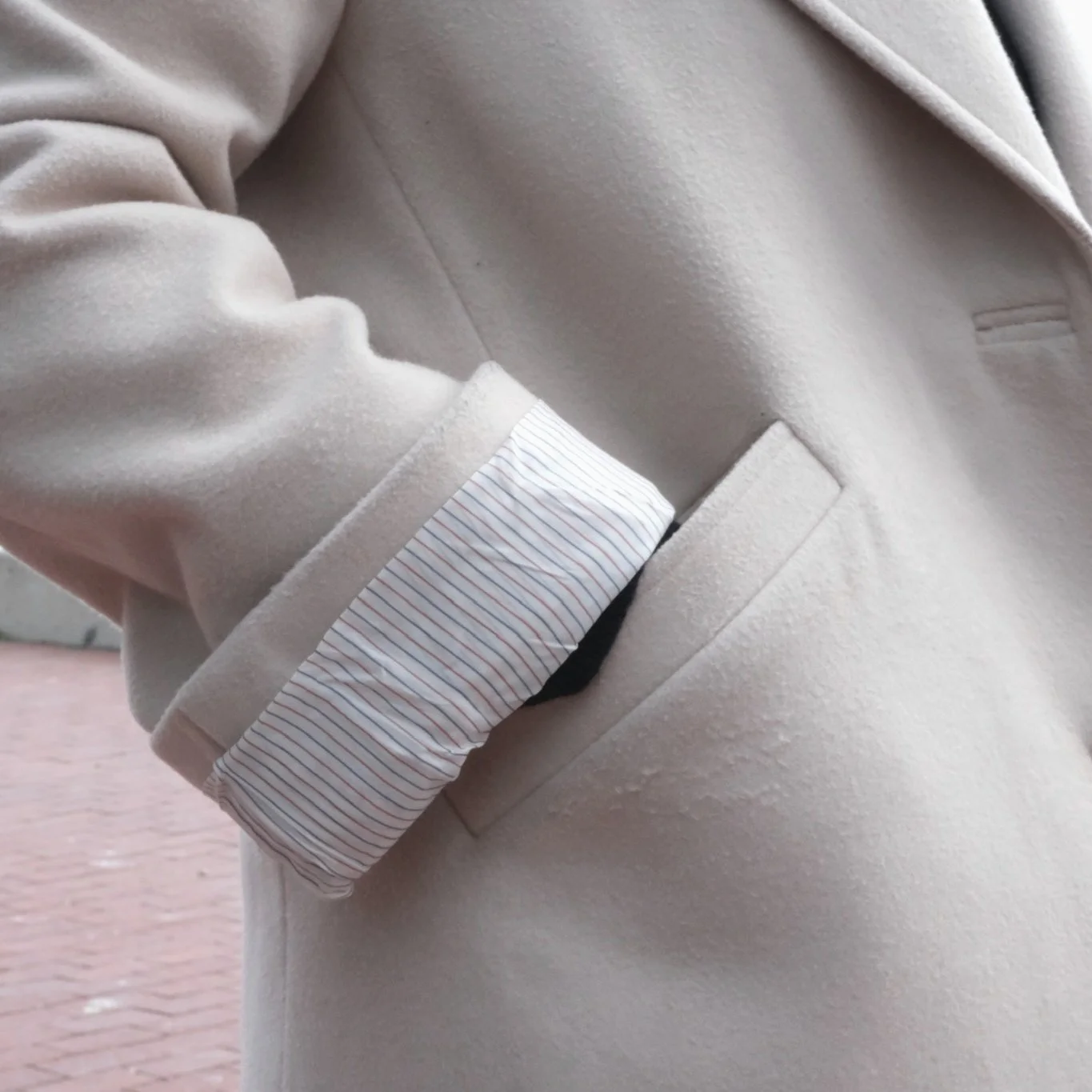 Close-up of a beige coat with a turned-up striped sleeve.