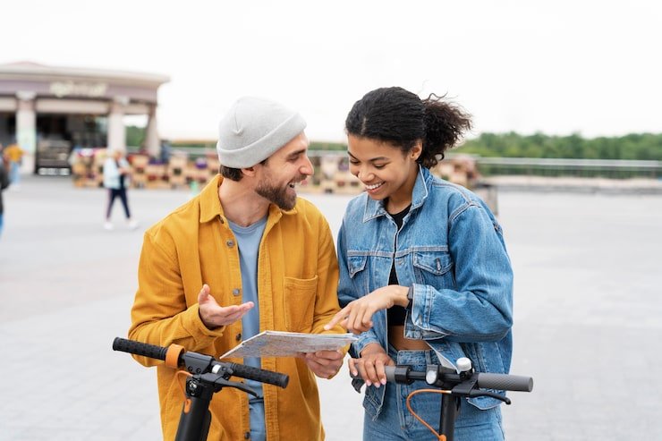 A young man and woman are smiling and talking while standing outdoors with electric scooters.