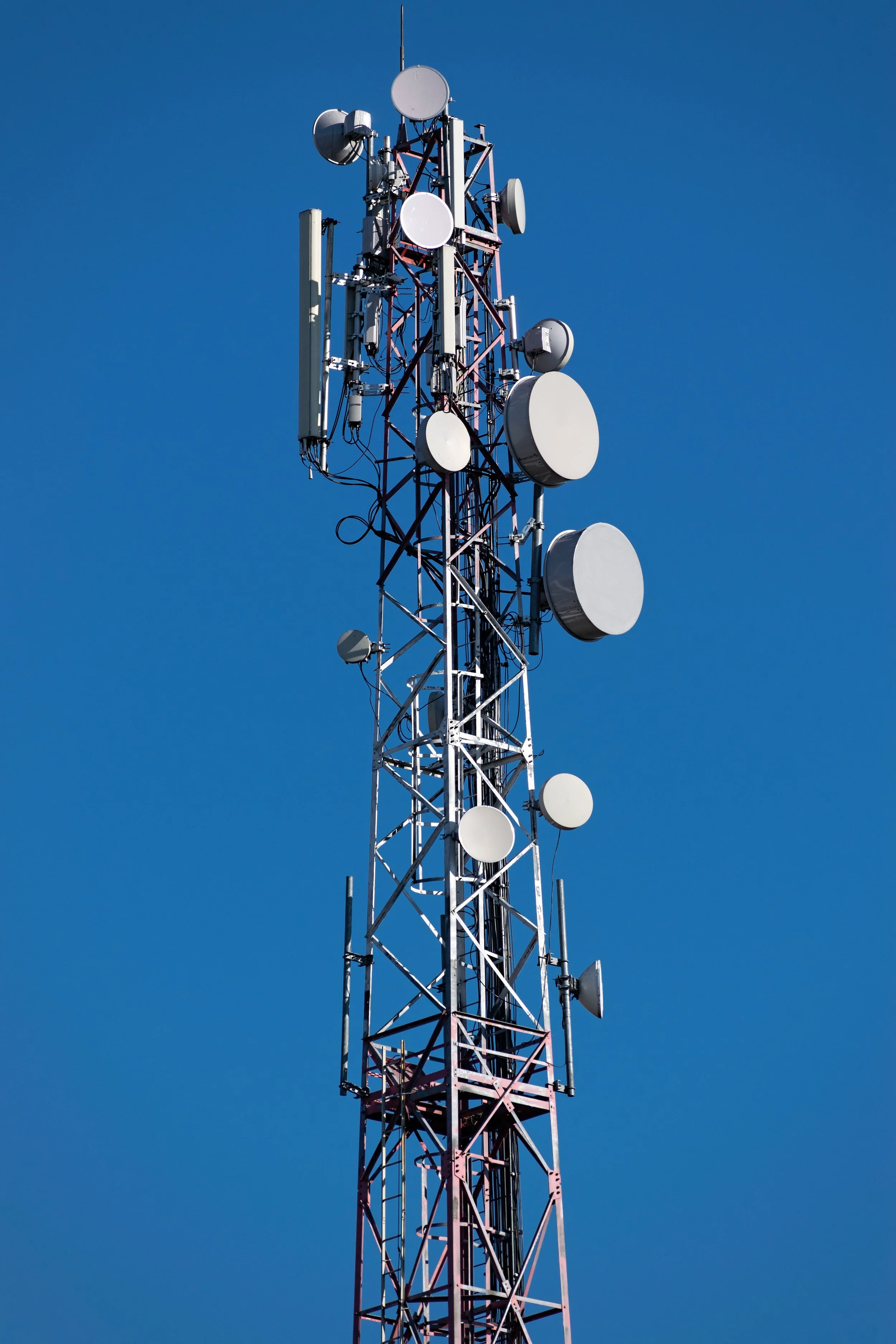 A tall telecommunications tower with various antennas and satellite dishes against a clear blue sky.