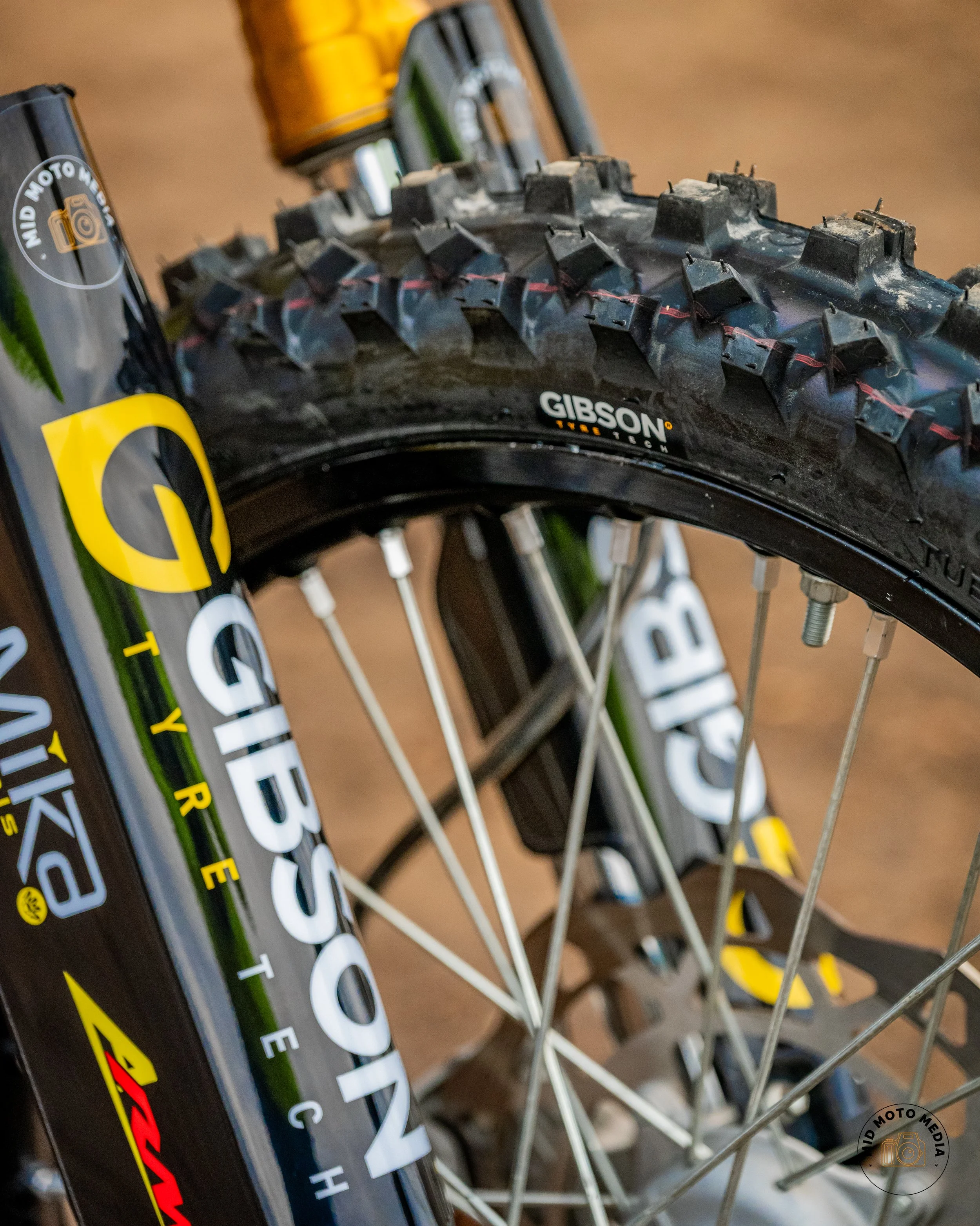 Close-up of a mountain bike's front wheel, showing the tire, rim, and spokes with various brand logos.