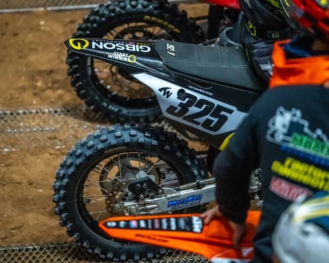 A dirt bike with the number 325 on its side, on the start gate, about to race motocross with riders lined up beside him.