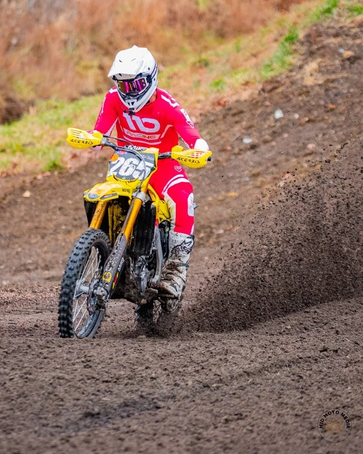 A person in red motocross gear, with a white helmet and goggles, riding a yellow dirt bike on a dirt track.