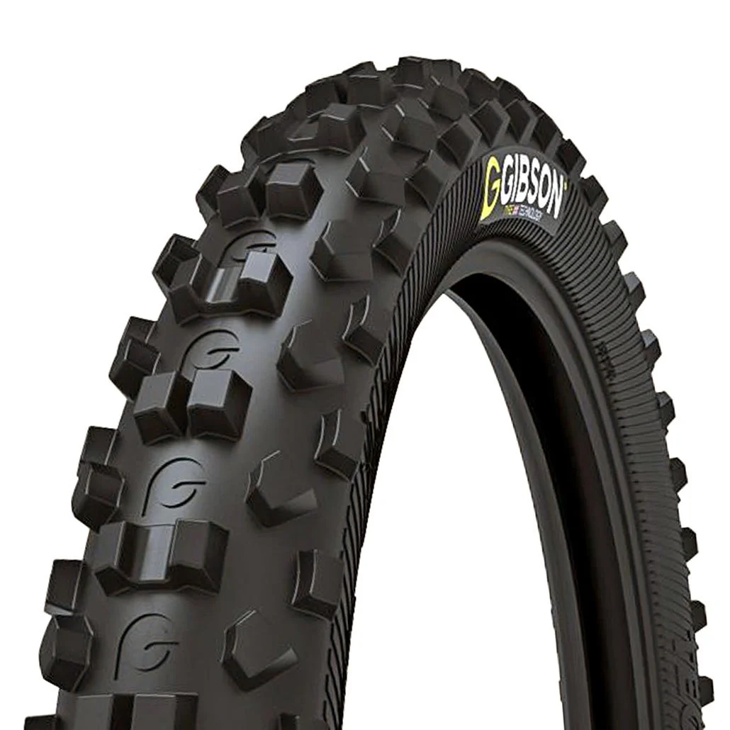 Close-up of a black off-road motorcycle tire with large tread blocks and the brand name Gibson visible on the sidewall.